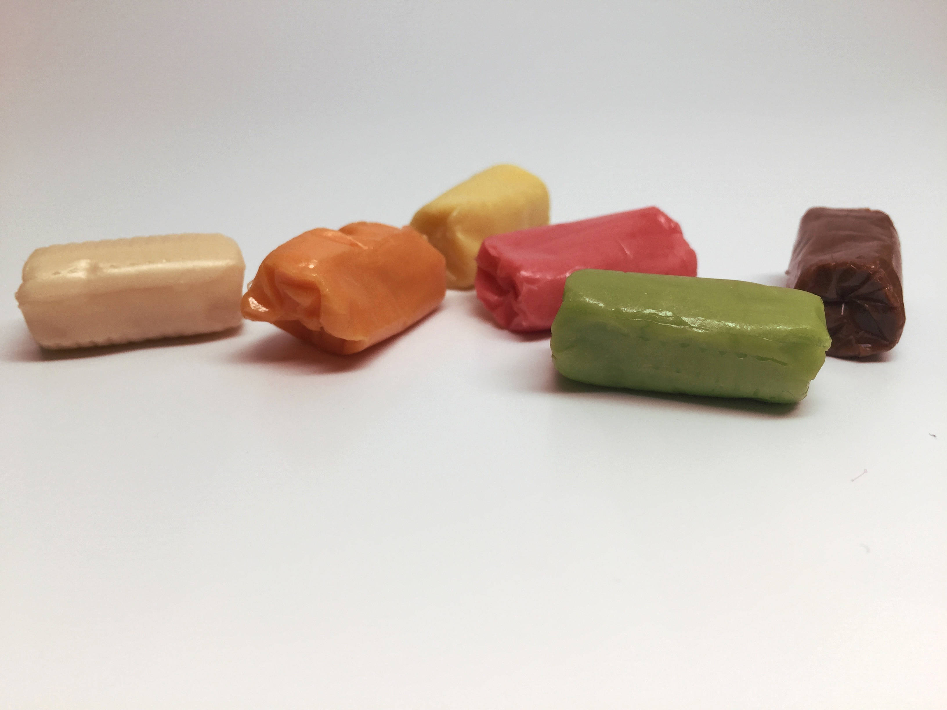chewy 桌布 壁紙 — 六顆色彩繽紛的包裝太妃糖，以不同色調隨意排列在純白表面上。