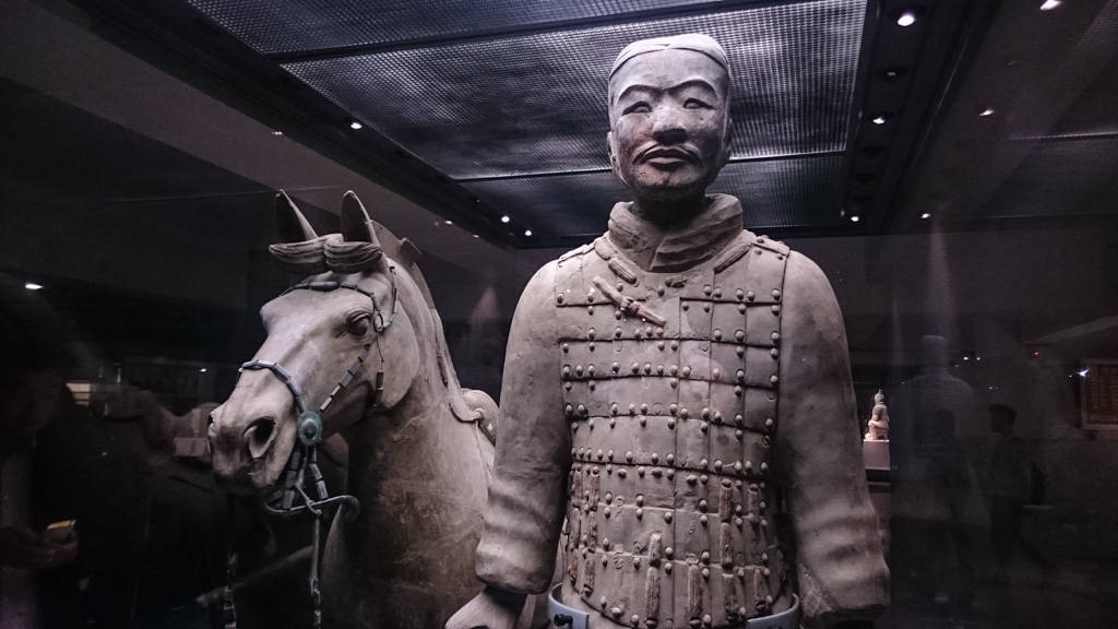 Xian 桌布 壁紙 — 兵馬俑及馬匹雕像在博物館燈光下展出，背景隱約可見參觀者。