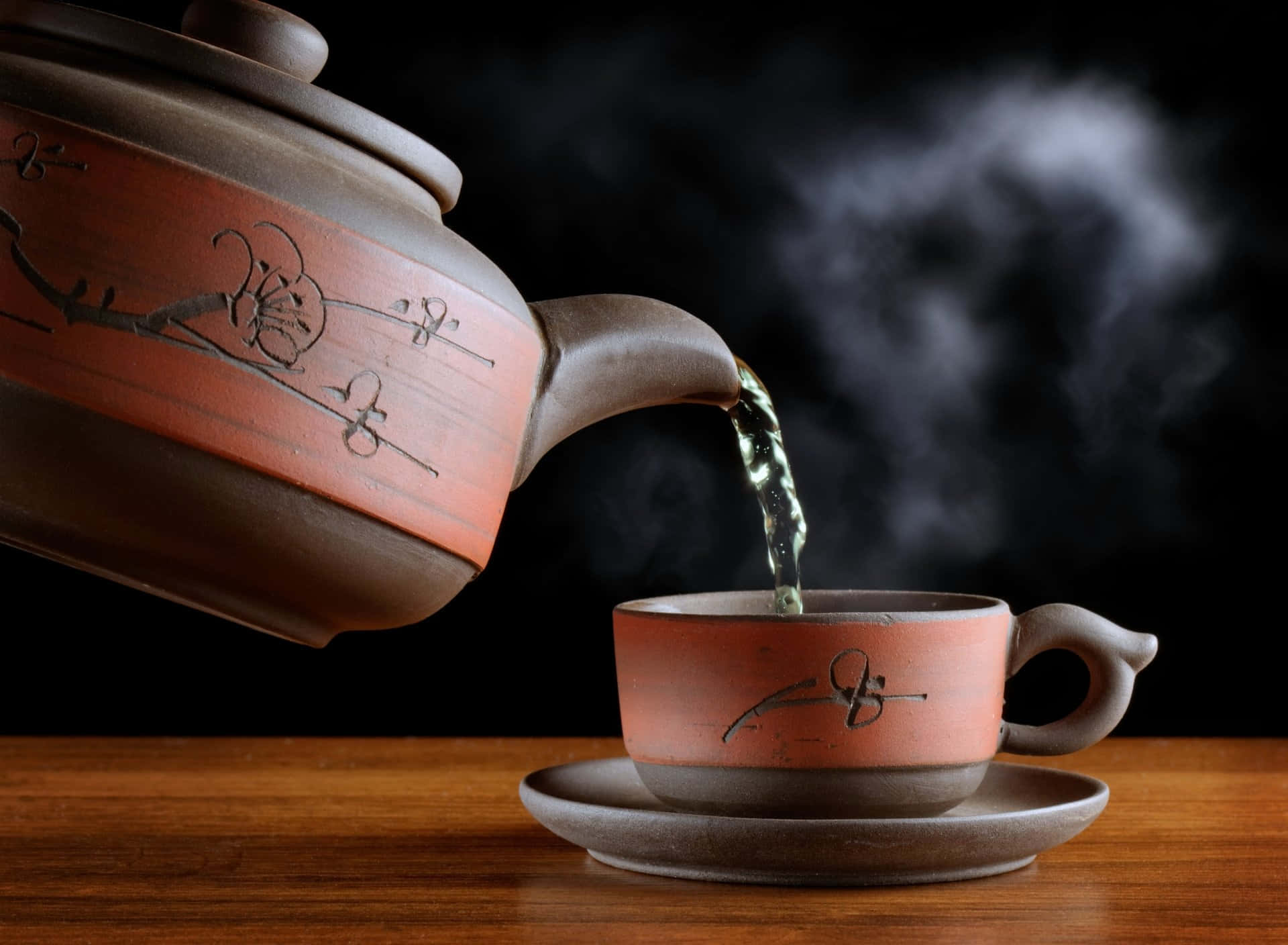 咖啡動圖 桌布 壁紙 — 冒煙的熱茶從陶瓷茶壺倒入相配的杯子中，放在木桌上，背景是深色。