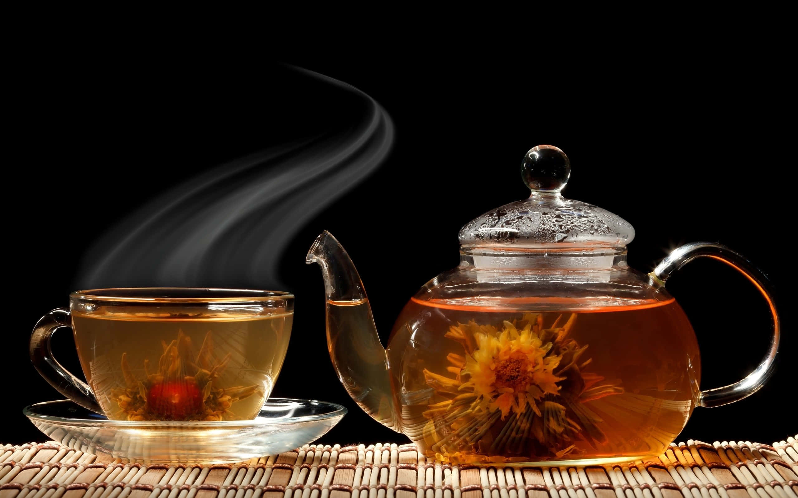 咖啡動圖 桌布 壁紙 — 冒煙的玻璃茶壺和杯子，盛開的花草茶花朵放在編織墊上，黑色背景。