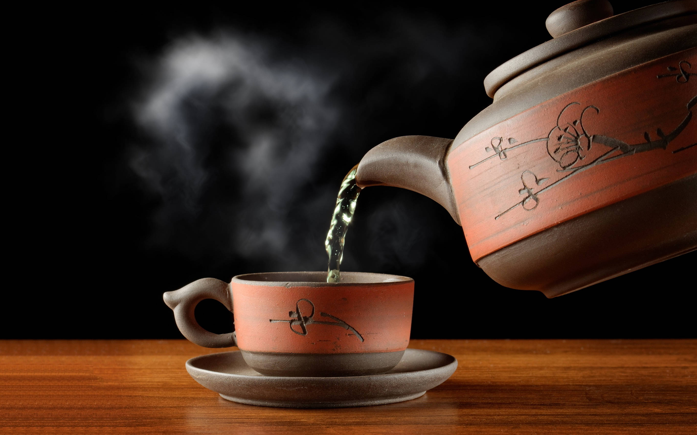 黑色 桌布 壁紙 — 冒煙的綠茶從陶瓷茶壺倒入相配的杯子中，放在木桌上，背景為黑色。