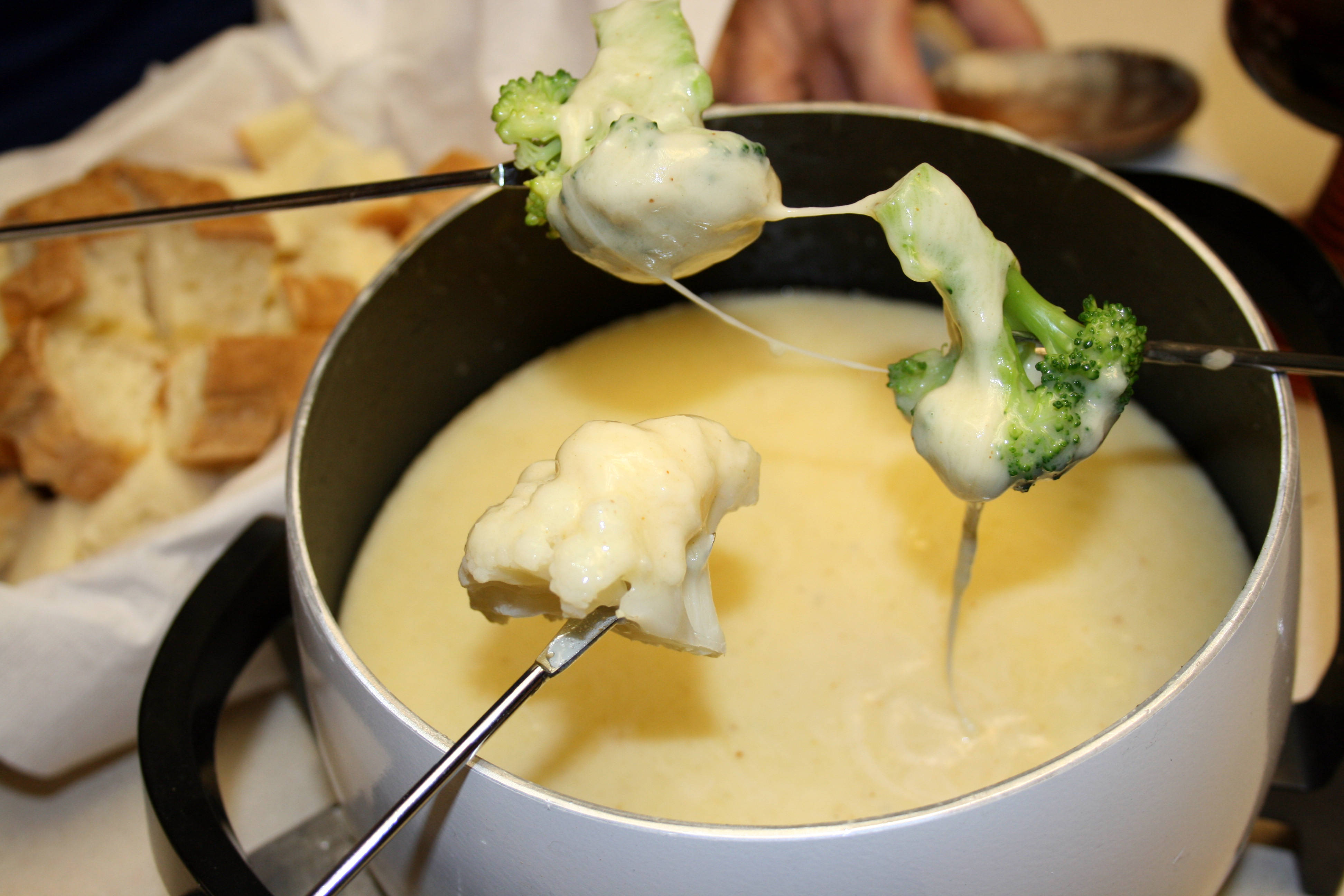 Cheese 桌布 壁紙 — 冒煙的起司火鍋，用長叉蘸青花菜和花椰菜，旁邊有一籃脆皮麵包。