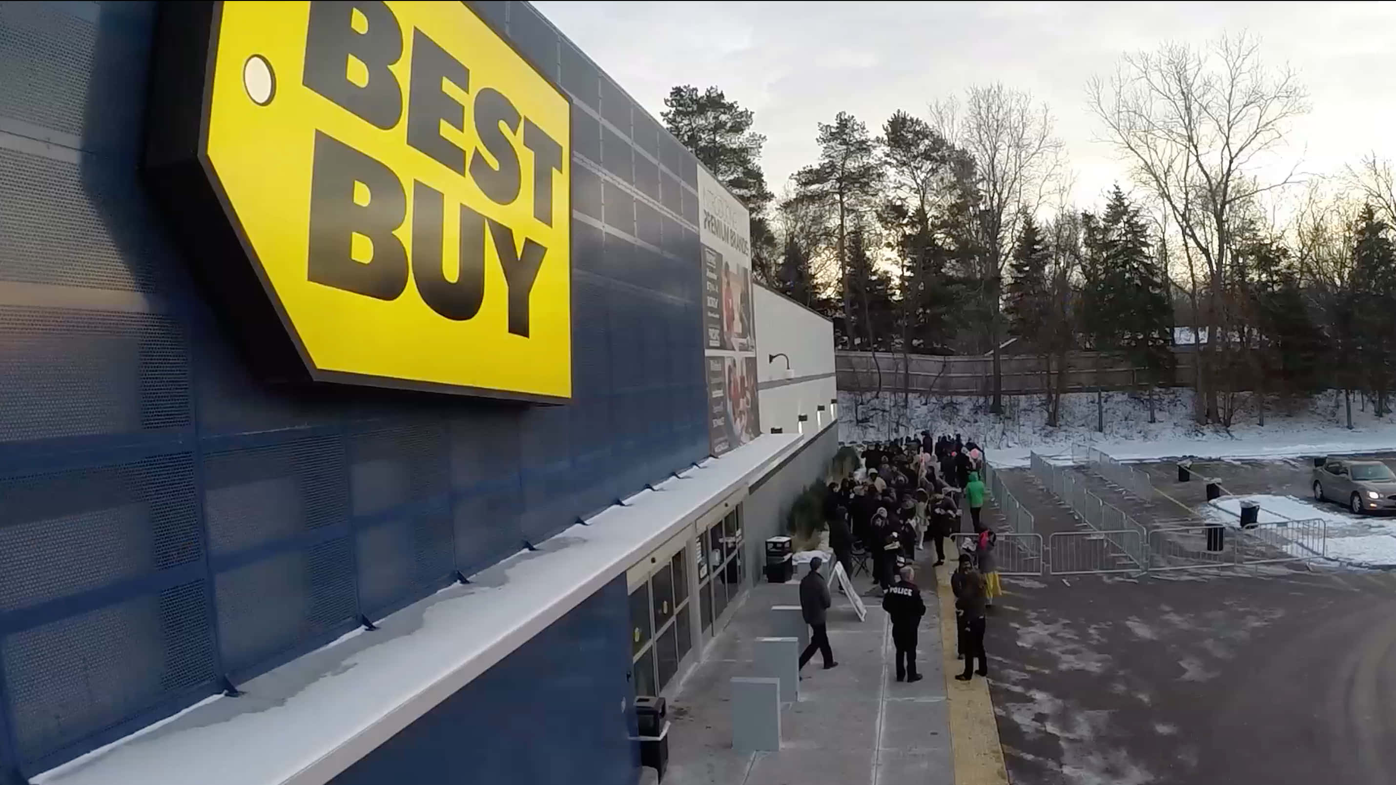 Best Buy 桌布 壁紙 — 冬季時，一群人在Best Buy商店外聚集，地上有積雪，背景是光禿禿的樹木。