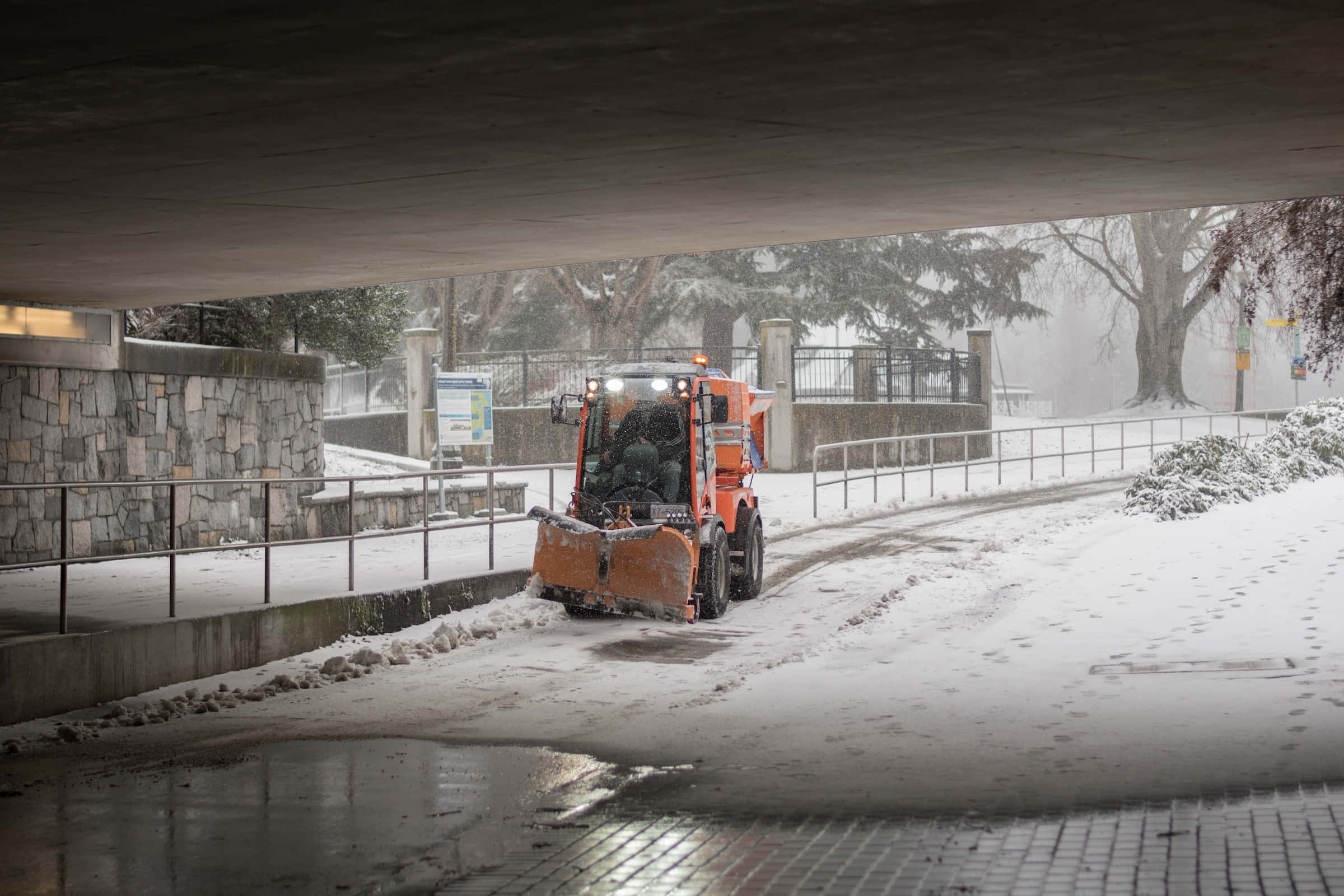 Snowplow 桌布 壁紙 — 冬季暴風雪期間，一輛橙色掃雪車在混凝土高架橋下清理積雪道路。