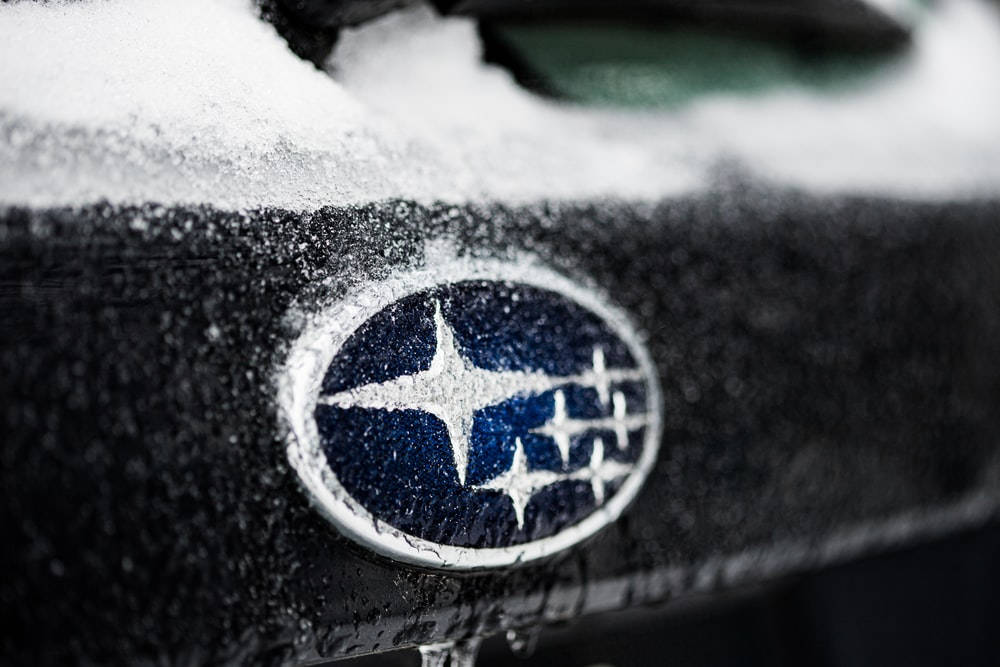 Subaru Logo 桌布 壁紙 — 冬季深色引擎蓋上沾滿新雪的Subaru標誌特寫。