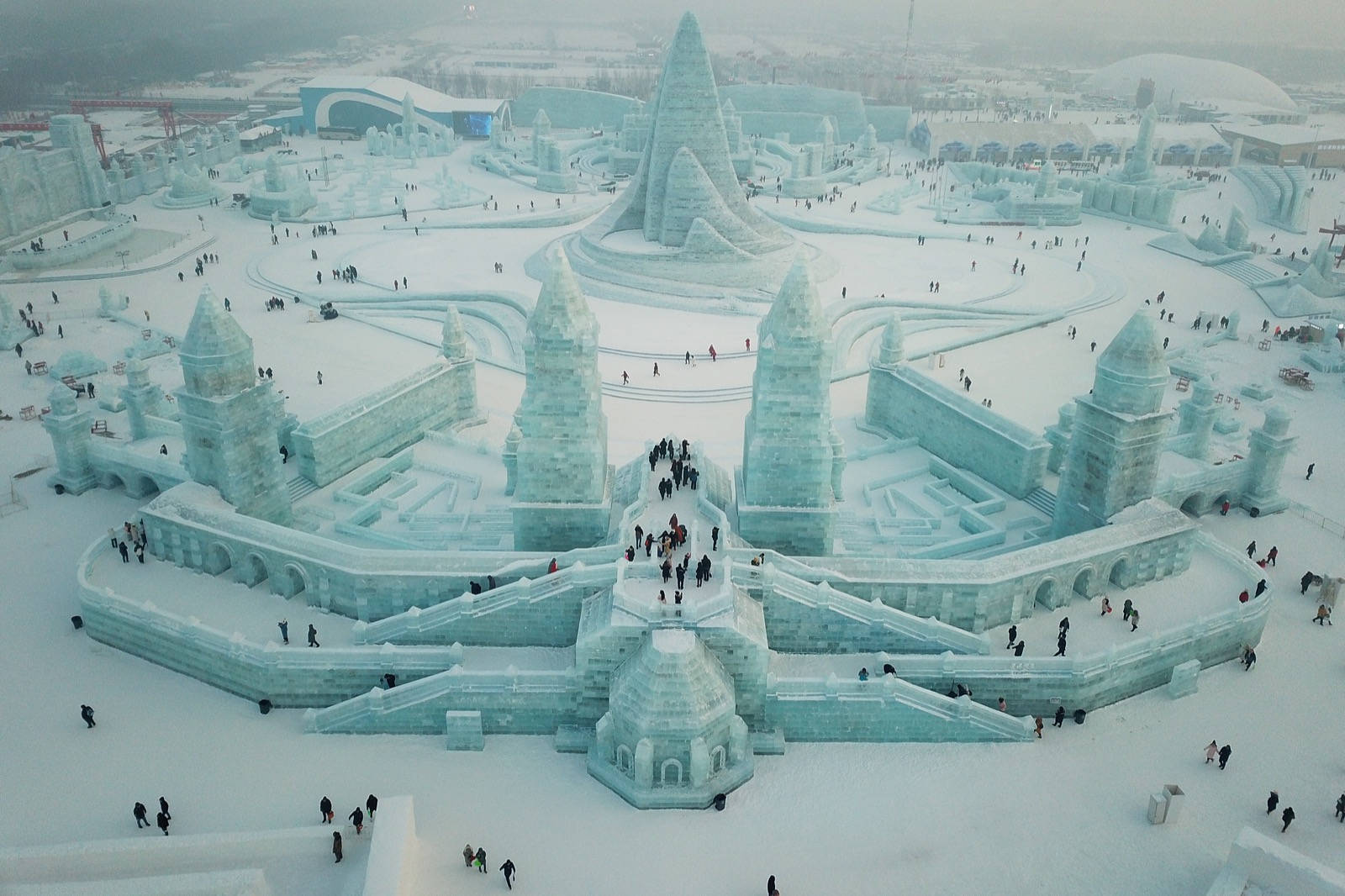 Harbin 桌布 壁紙 — 冬季節日中，遊客探索白雪覆蓋小徑的巨大而複雜的冰城堡雕塑的鳥瞰圖。
