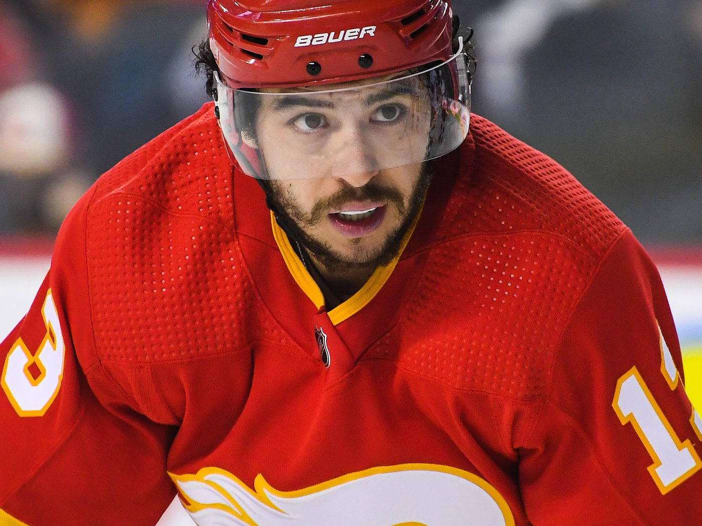 hockey 桌布 壁紙 — 冰上比賽期間，一名身穿紅色球衣和頭盔、專注的冰球運動員的特寫。