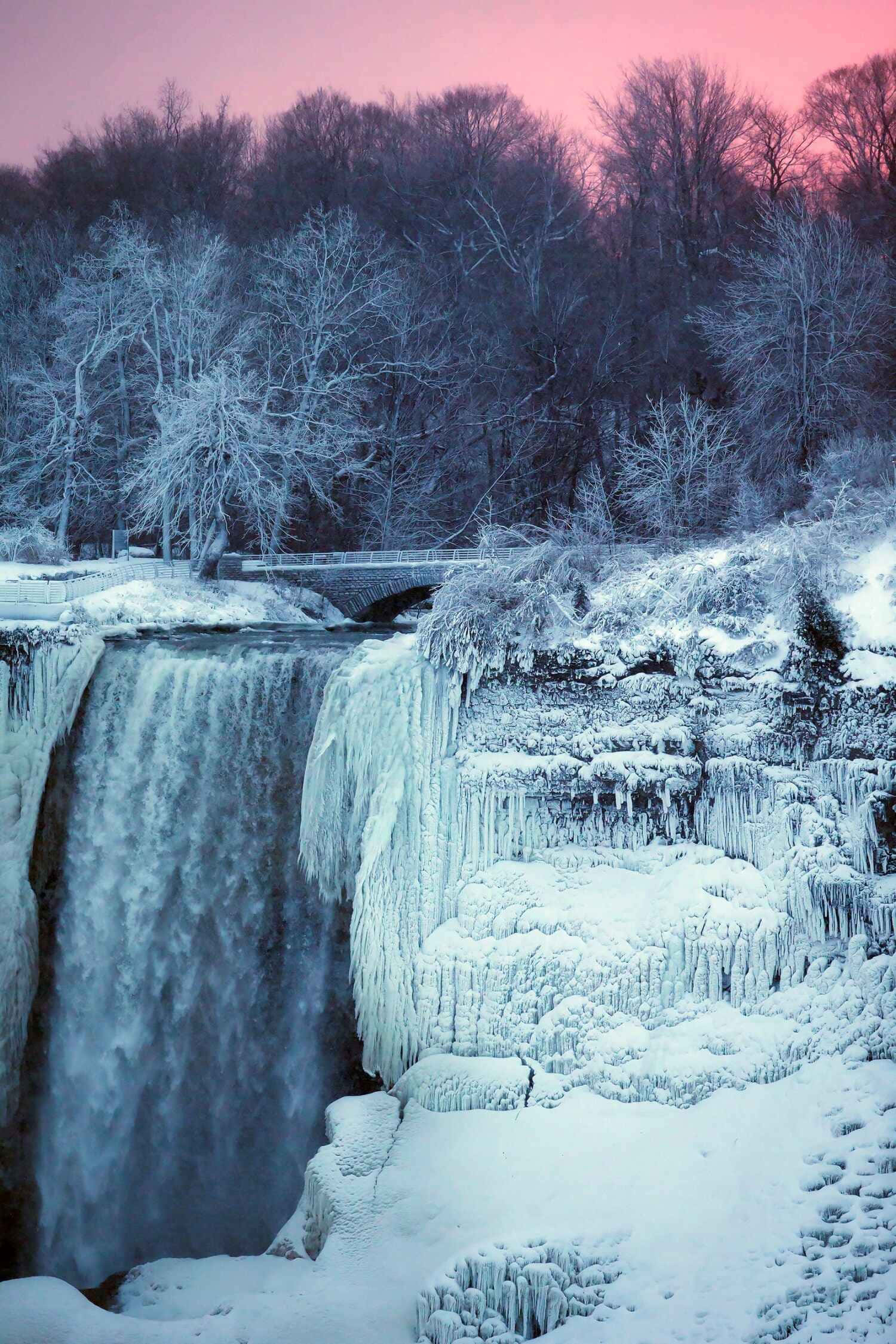Niagara Falls 桌布 壁紙 — 冰凍瀑布在粉紅色暮色天空下流過冰崖，周圍有積雪的樹木。