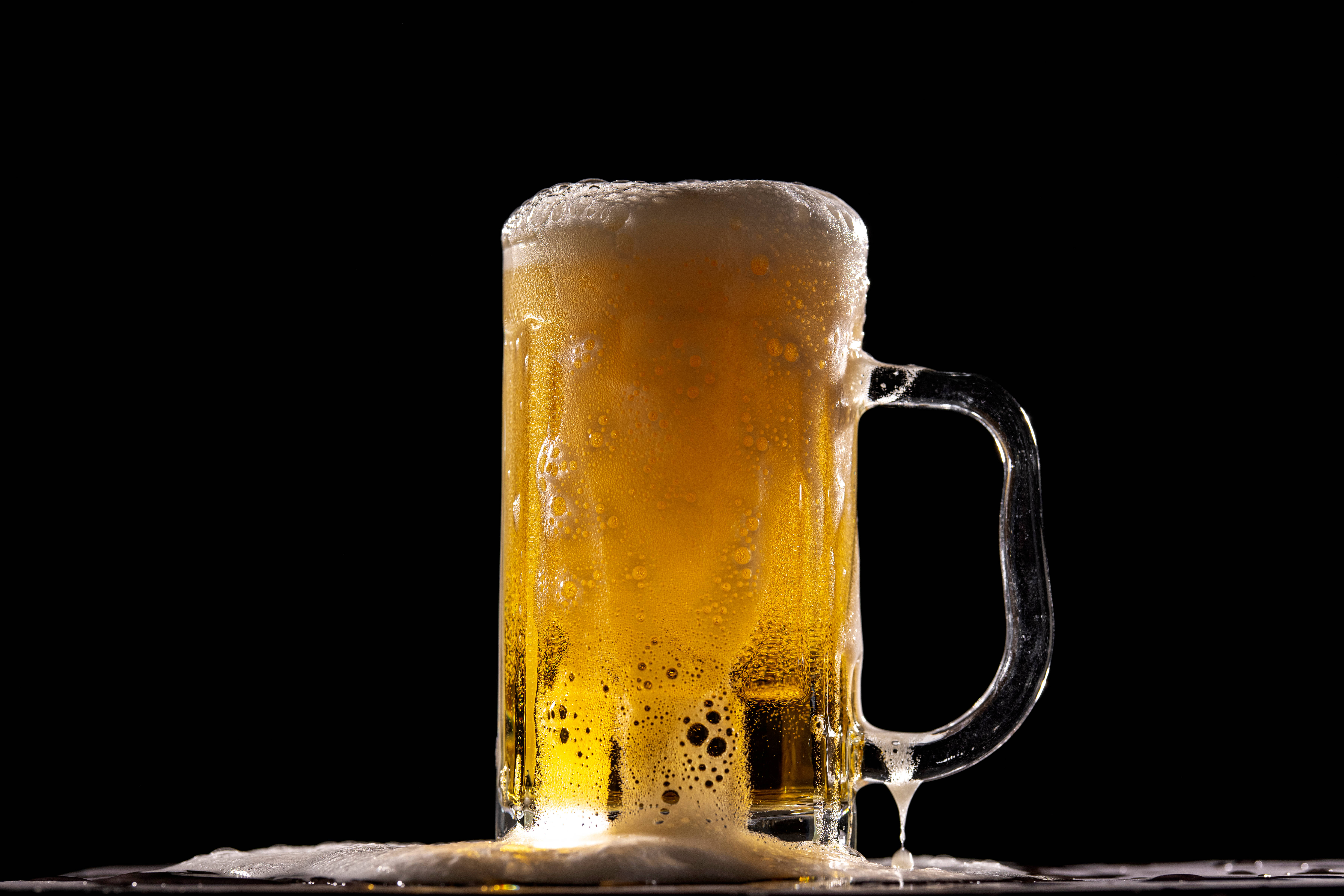 Beer 桌布 壁紙 — 冰凍琥珀色啤酒杯，帶有泡沫頂部和冷凝水滴，襯托在純黑背景上。
