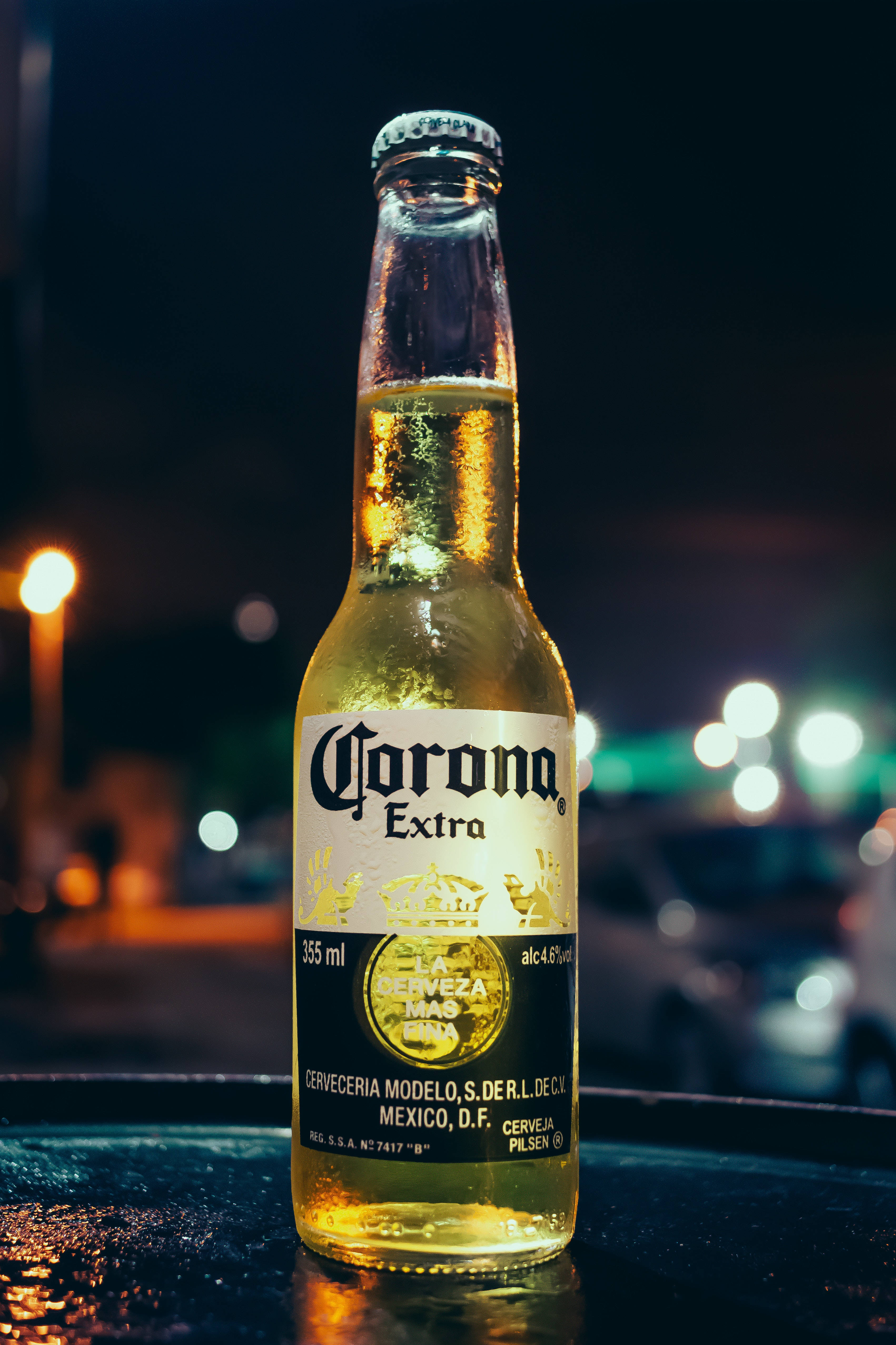 alcohol 桌布 壁紙 — 冰凍的Corona Extra啤酒瓶在夜晚城市燈光下的暗桌上閃爍著冷凝水珠。