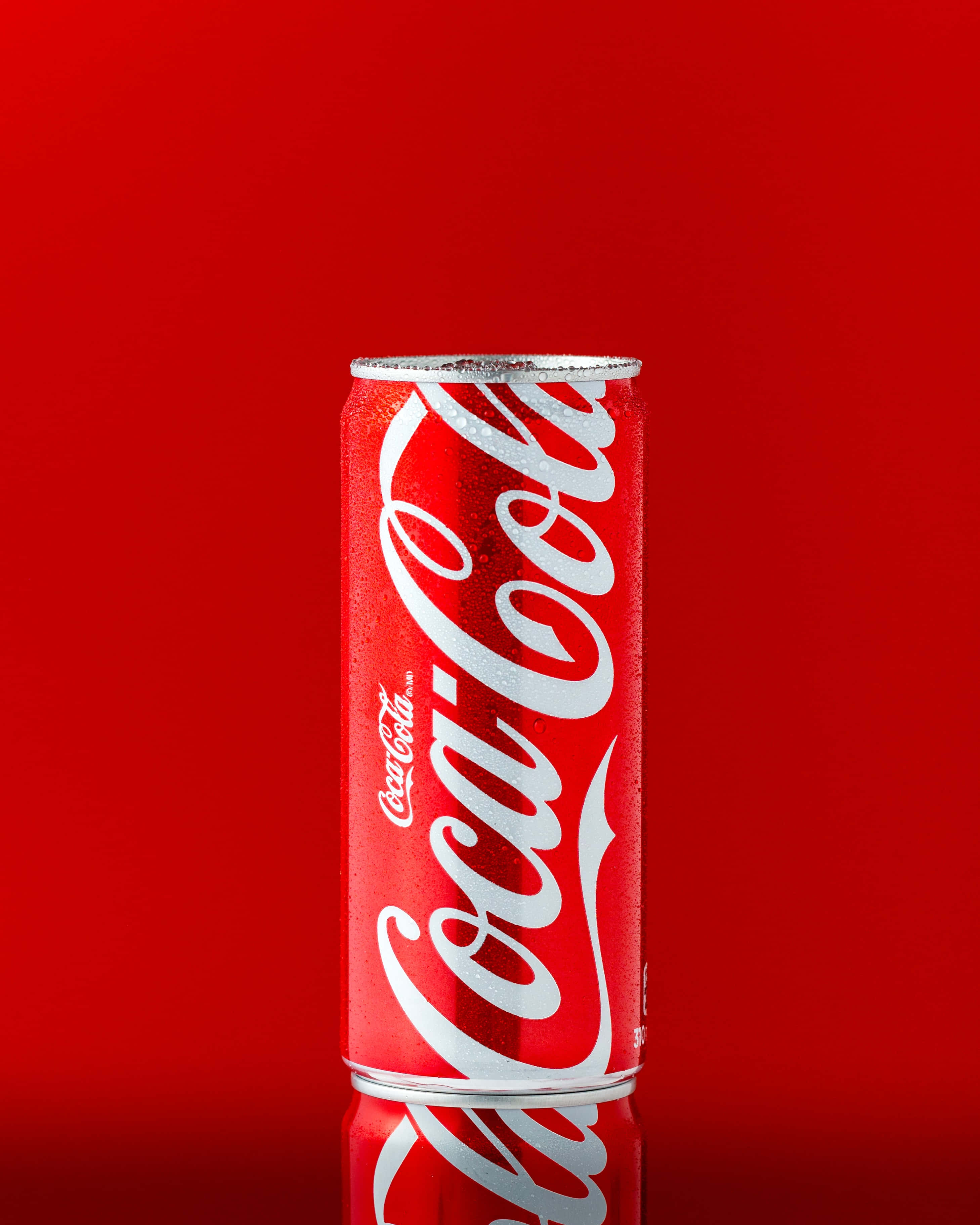 coca cola 桌布 壁紙 — 冰凍的可口可樂罐上凝結的水珠在純紅色背景及下方反光表面上閃閃發光。