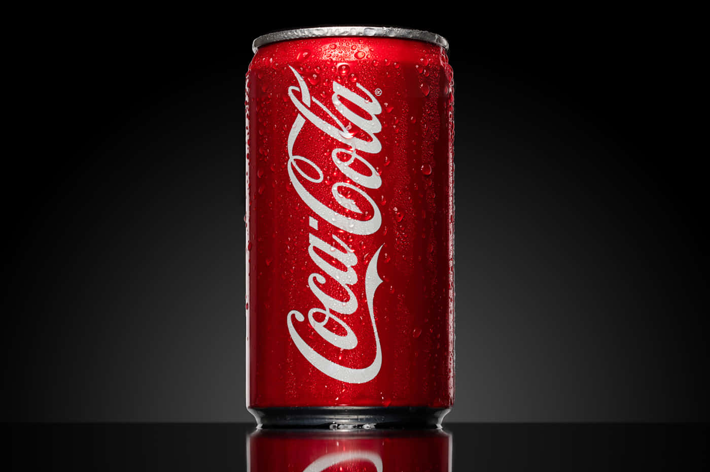 coca cola 桌布 壁紙 — 冰凍的可口可樂罐帶有冷凝水滴，在帶有反射表面的深色漸變背景上閃閃發光。