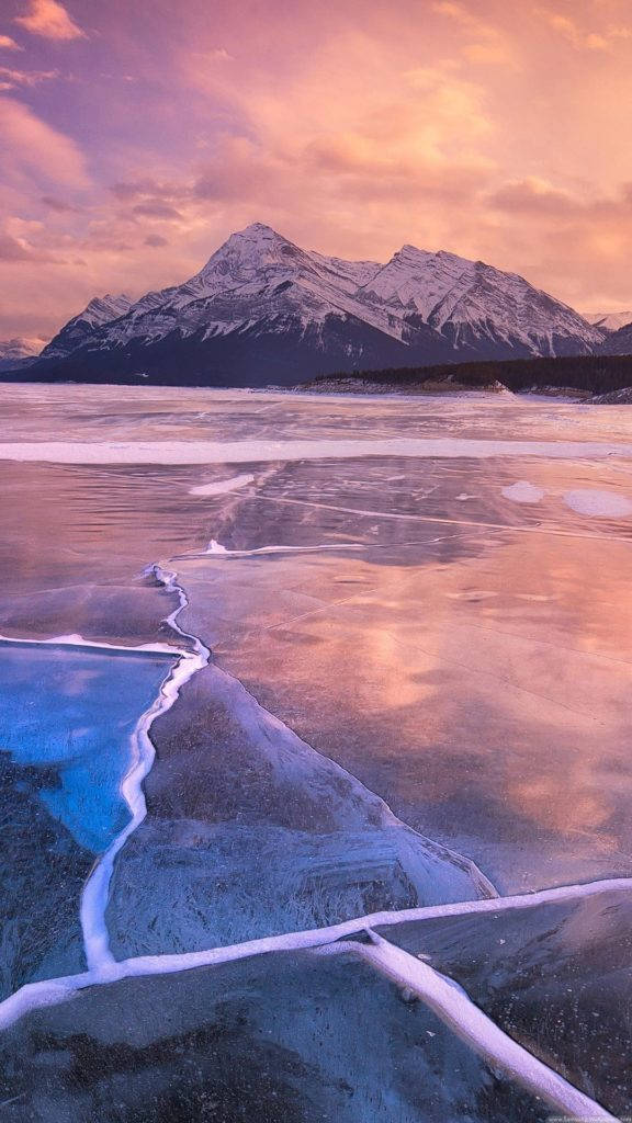 Nature iPhone 桌布 壁紙 — 冰凍的湖面反射出雪山上空充滿活力的粉紅色和橙色日落天空。
