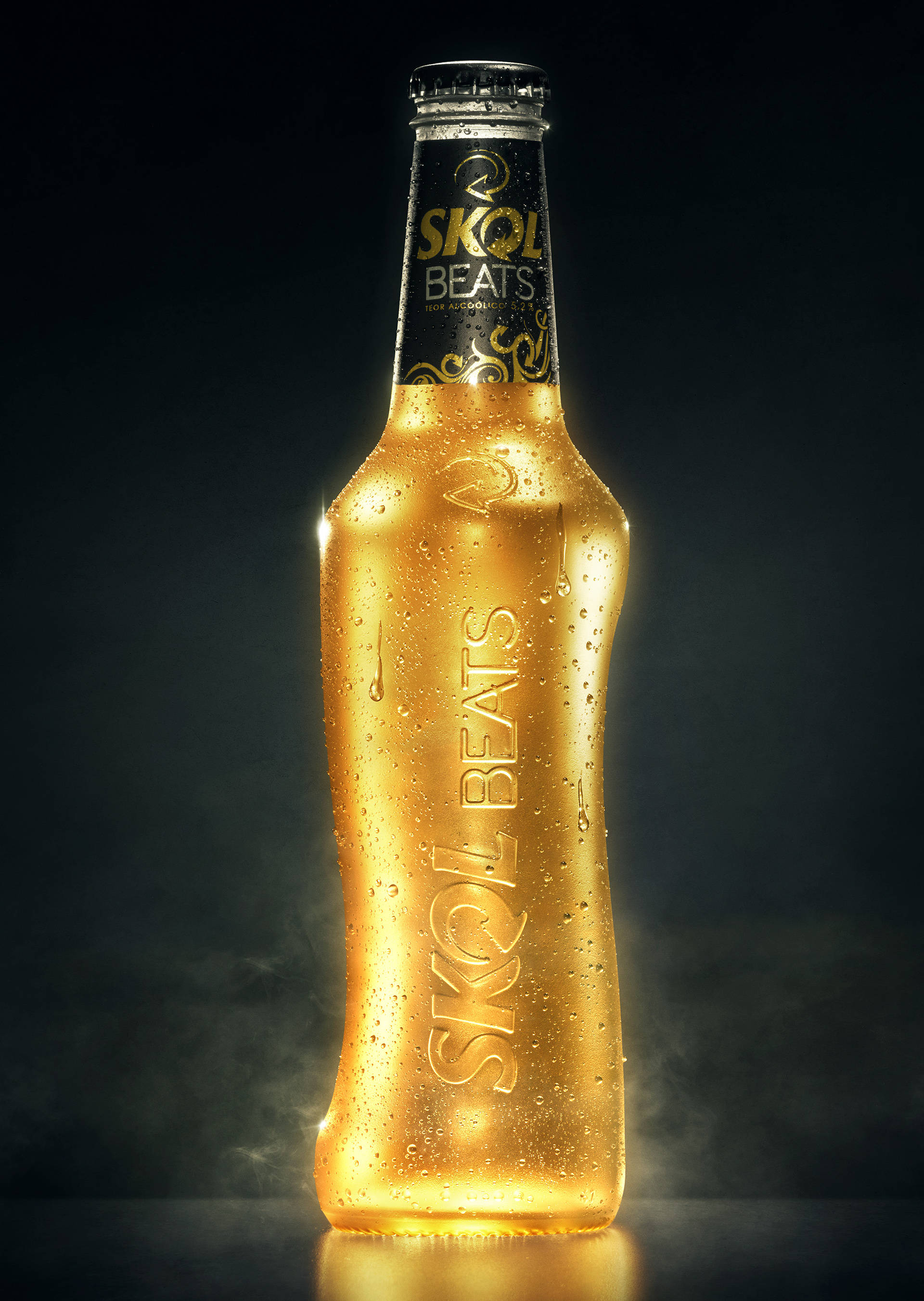bottle 桌布 壁紙 — 冰凍的金色Skol Beats啤酒瓶在黑暗煙霧背景上閃爍著冷凝水珠。