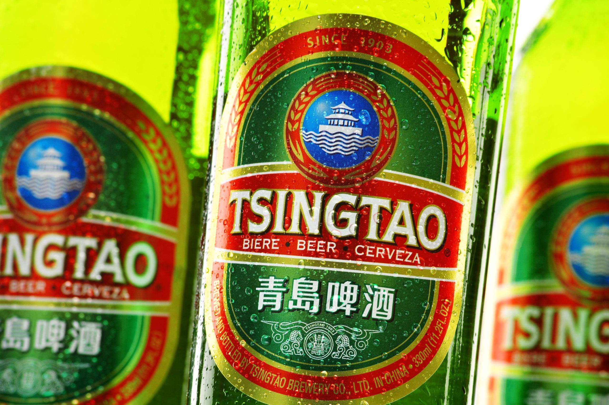 booze 桌布 壁紙 — 冰凍青島啤酒瓶的特寫，瓶身凝結的水珠在明亮燈光下閃閃發光。
