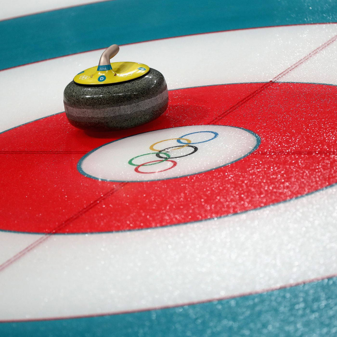 Olympics 桌布 壁紙 — 冰壺石特寫，停留在光澤冰場上的紅色奧運環靶心上。