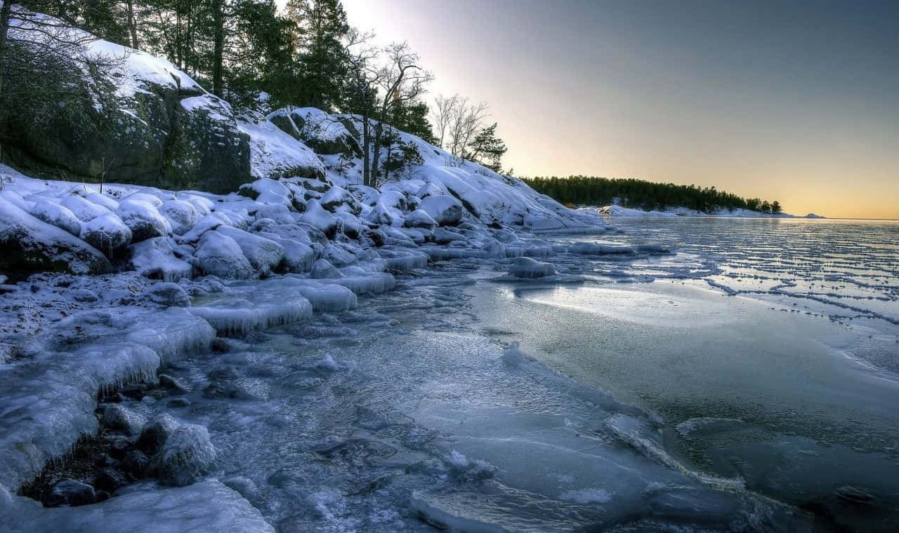 Frozen Lake 桌布 壁紙 — 冰封的海岸線，冰石和積雪覆蓋的樹木在暮色天空下。