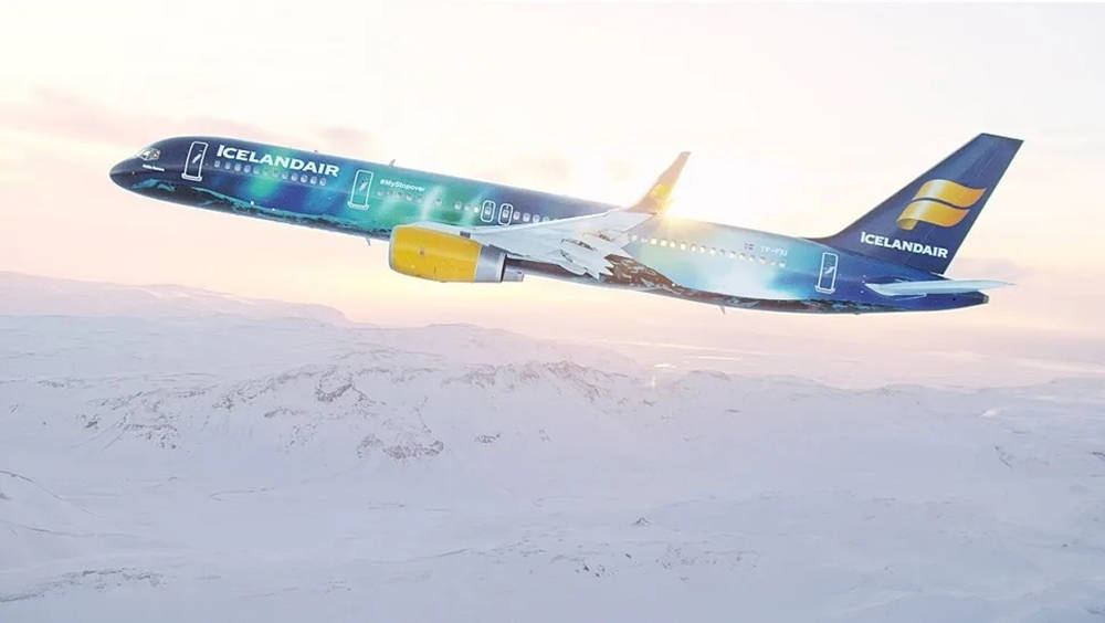 飛機 桌布 壁紙 — 冰島航空飛機帶有鮮豔的藍、綠和黃色塗裝，在日出時翱翔於積雪覆蓋的山脈之上。