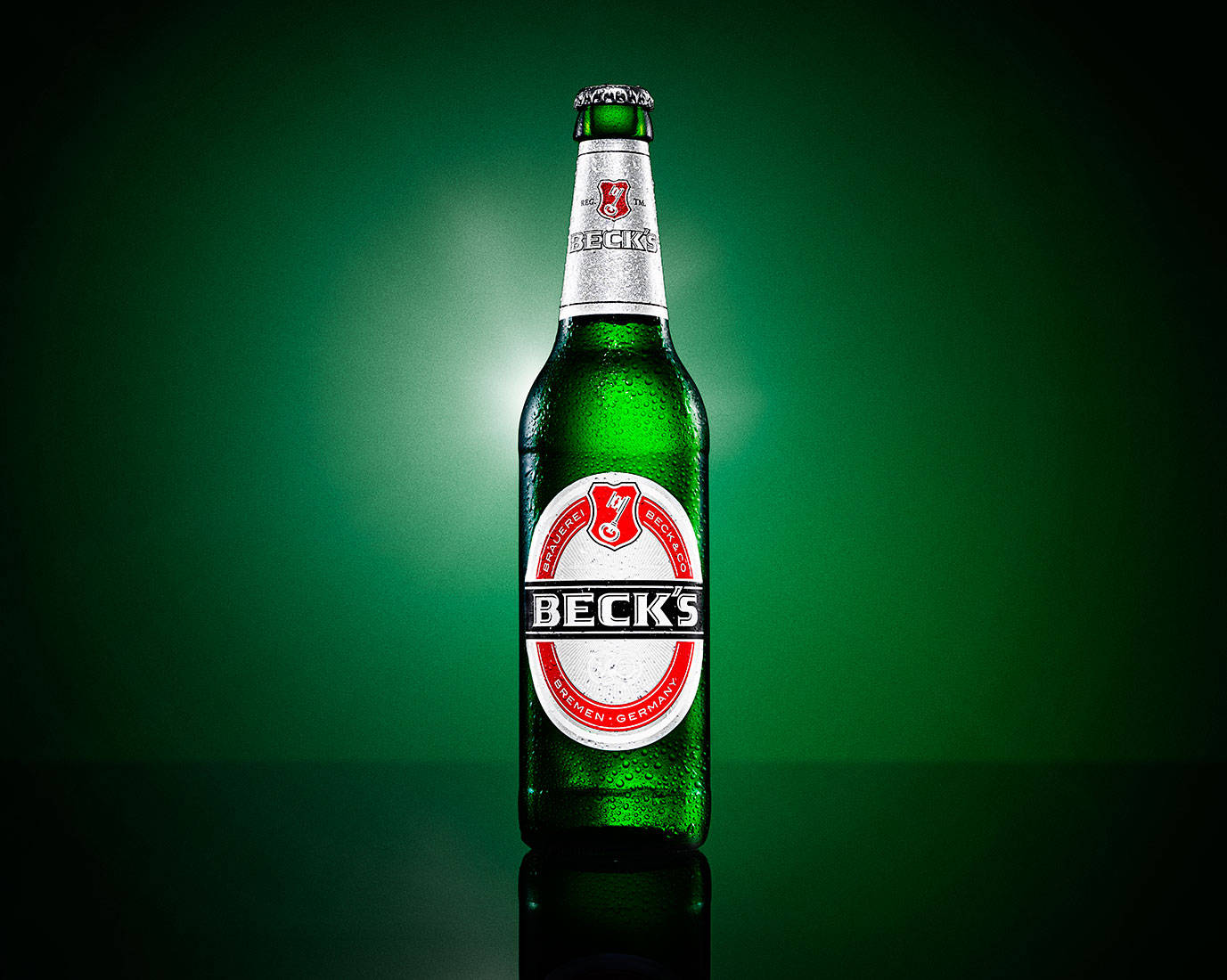 Beer 桌布 壁紙 — 冰涼的 Beck's 啤酒瓶在深綠色漸層背景和柔和聚光燈下閃爍著冷凝水珠。