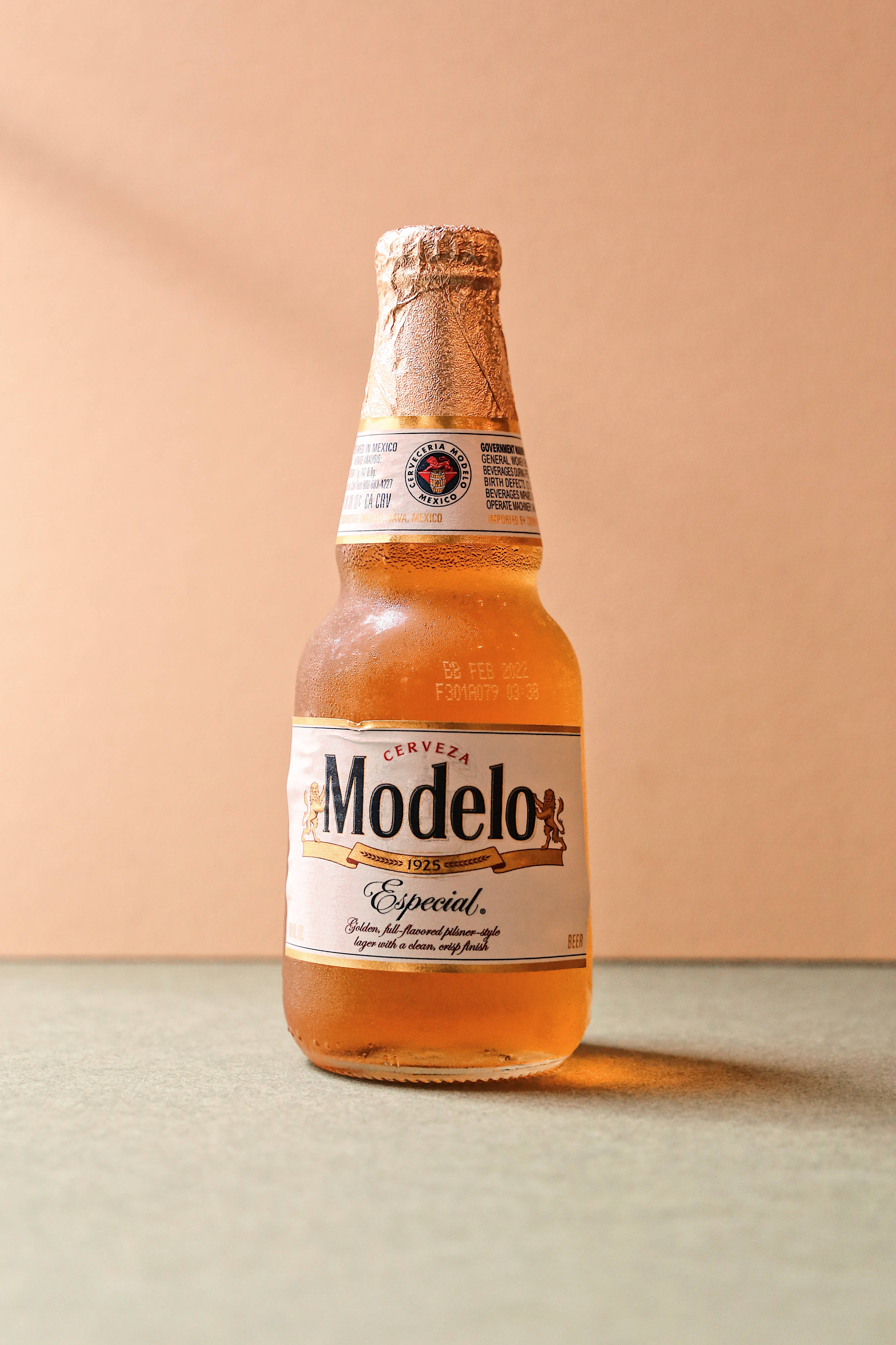 酷炫iPhone 桌布 壁紙 — 冰涼的Modelo Especial啤酒瓶在溫暖的蜜桃色背景下閃爍著冷凝水珠。