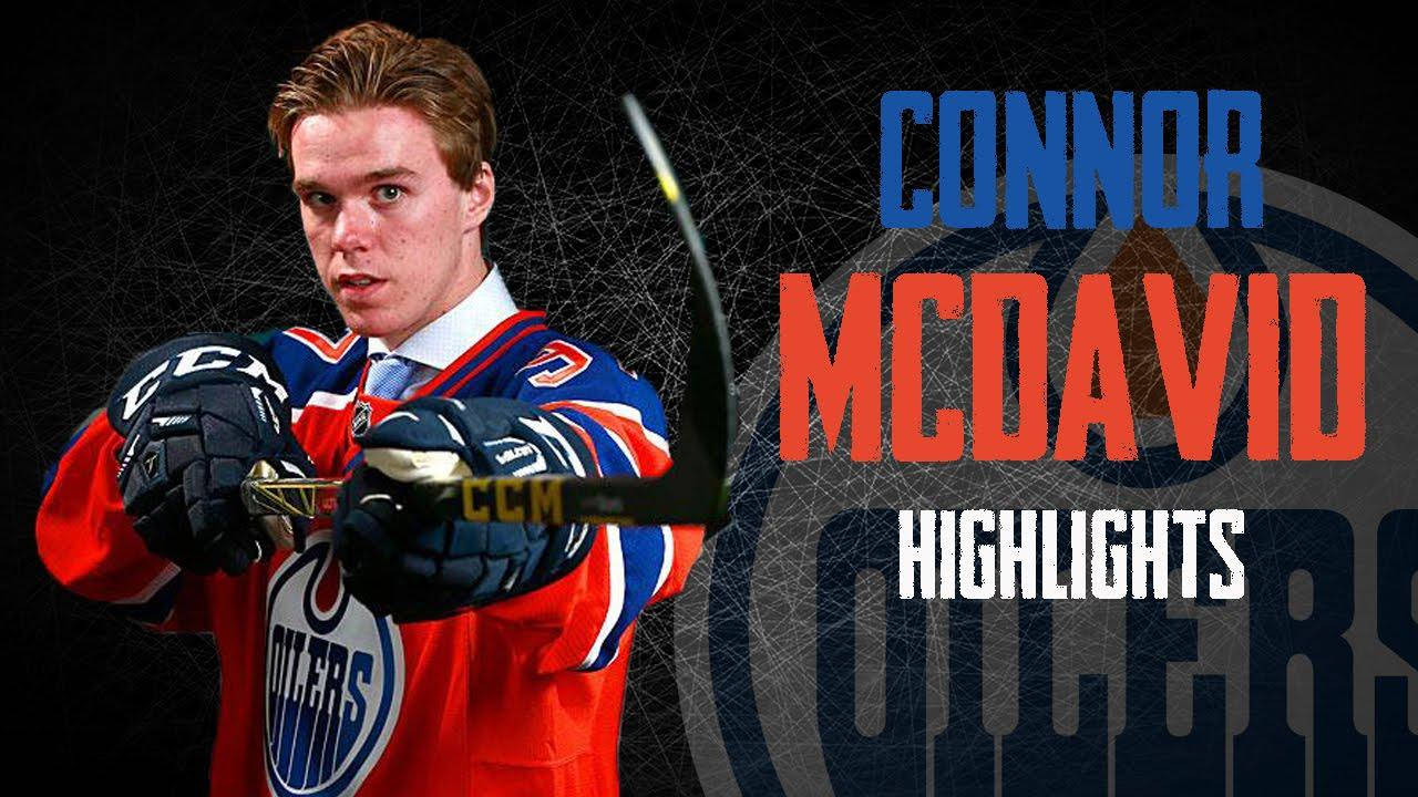 hockey 桌布 壁紙 — 冰球球員 Connor McDavid 身穿 Edmonton Oilers 球衣，在深色網狀背景上手持球棍準備行動，並配有粗體文字。