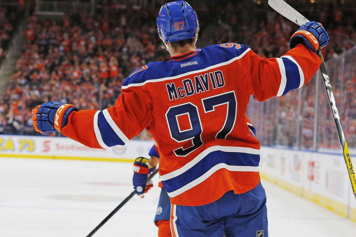 hockey 桌布 壁紙 — 冰球運動員 Connor McDavid 身穿橙色藍色 97 號球衣，在冰上高舉雙臂，面對歡呼的人群慶祝。