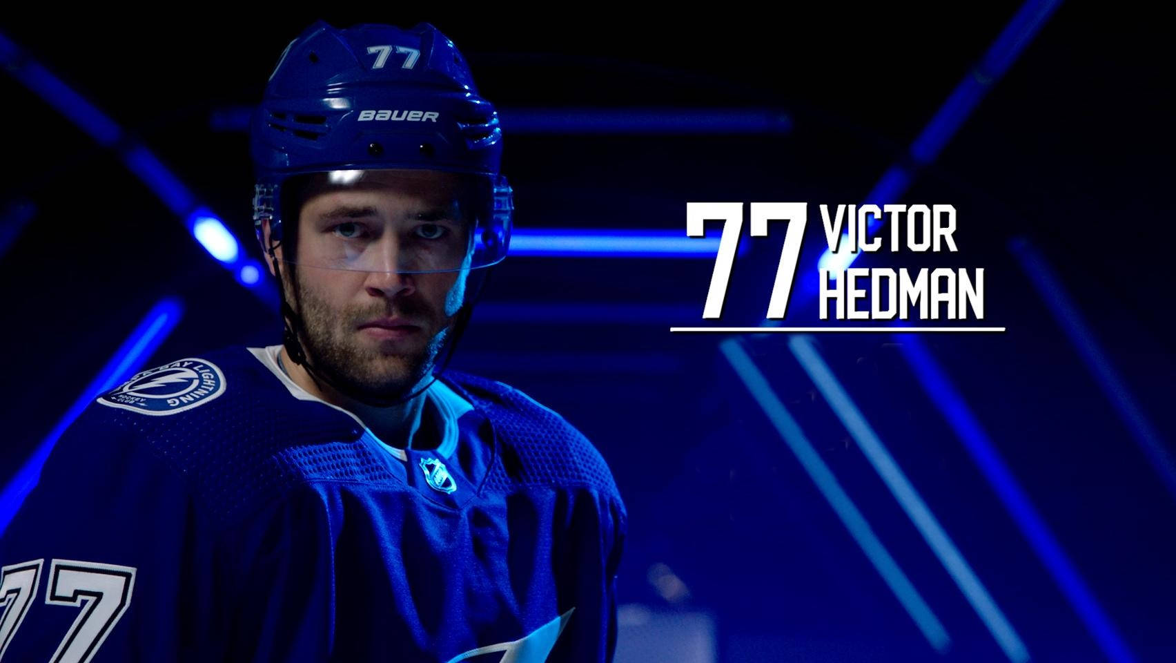 hockey 桌布 壁紙 — 冰球運動員 Victor Hedman 身穿藍色裝備，在戲劇性的藍色燈光下，背景有發光的條紋，他專注地凝視著。