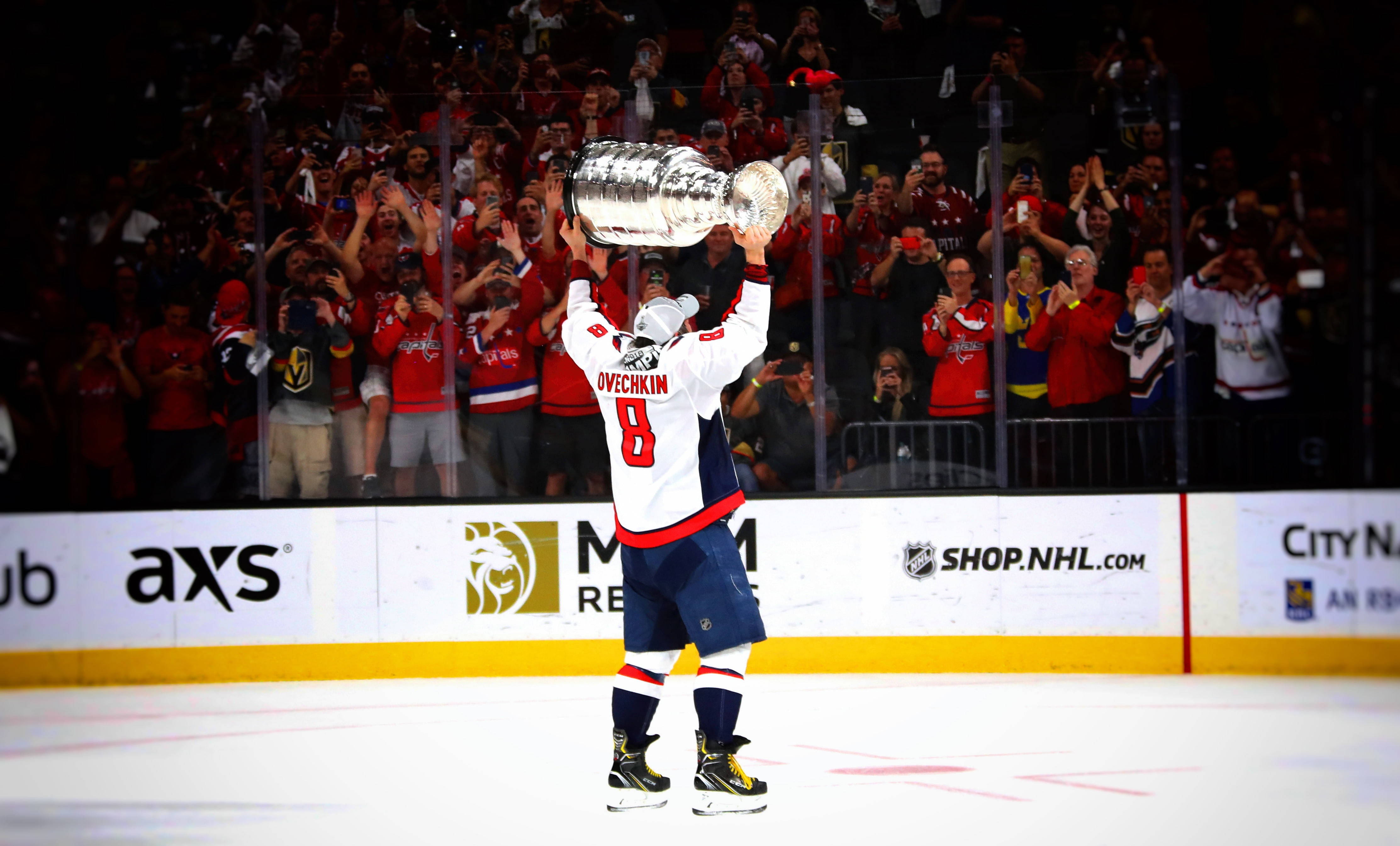 hockey 桌布 壁紙 — 冰球運動員奧維奇金在冰上高舉史丹利盃，勝利的姿態令玻璃後熱情的球迷歡呼不已。