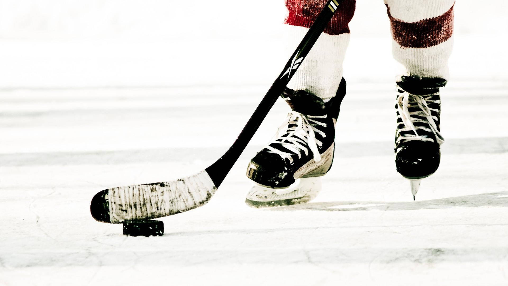 hockey 桌布 壁紙 — 冰球運動員的溜冰鞋和球桿在明亮冰場上準備擊球的特寫。