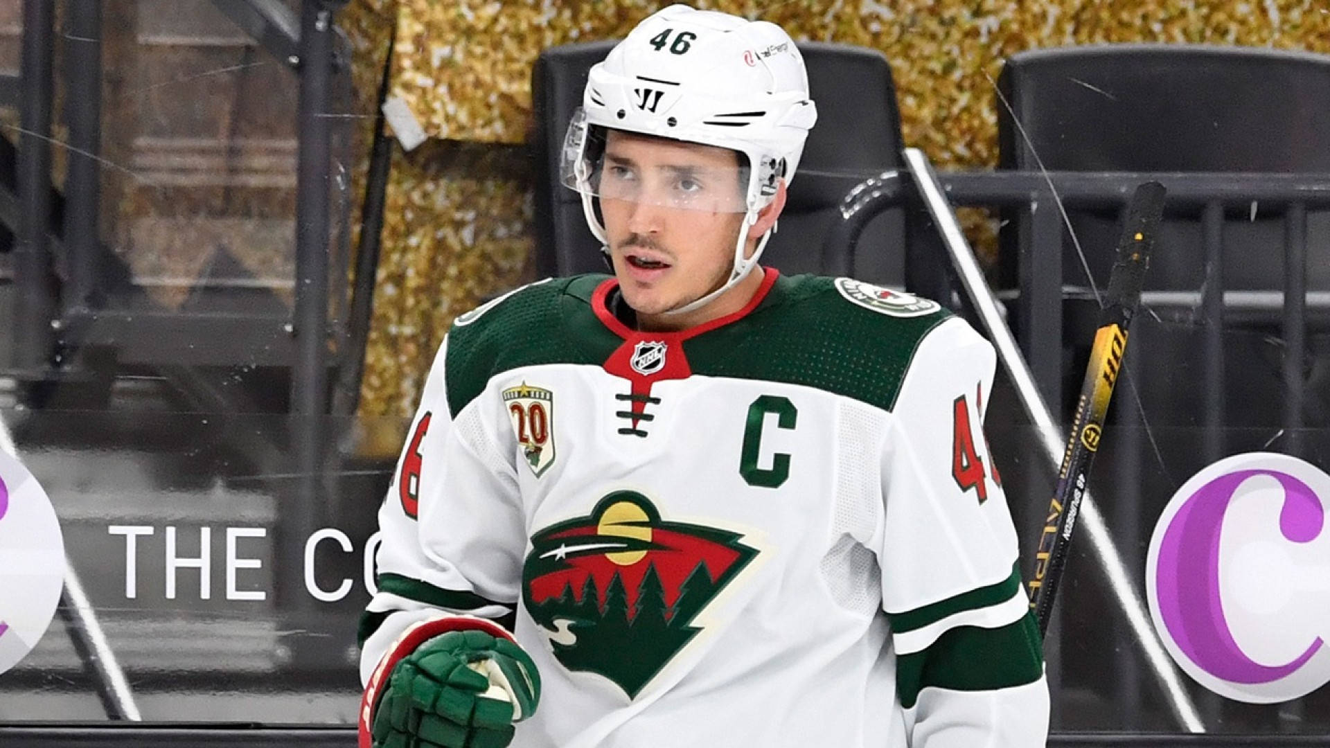 hockey 桌布 壁紙 — 冰球運動員身穿白色、綠色和紅色的明尼蘇達荒野隊球衣，帶有隊長C，站在冰場上。