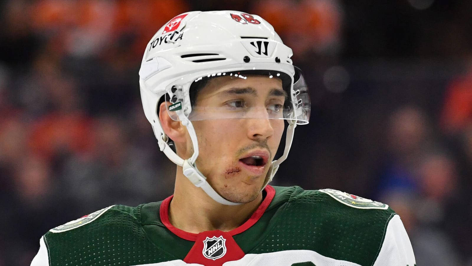 hockey 桌布 壁紙 — 冰球運動員近距離特寫，身穿綠色和白色裝備，比賽中嘴唇有明顯傷口。