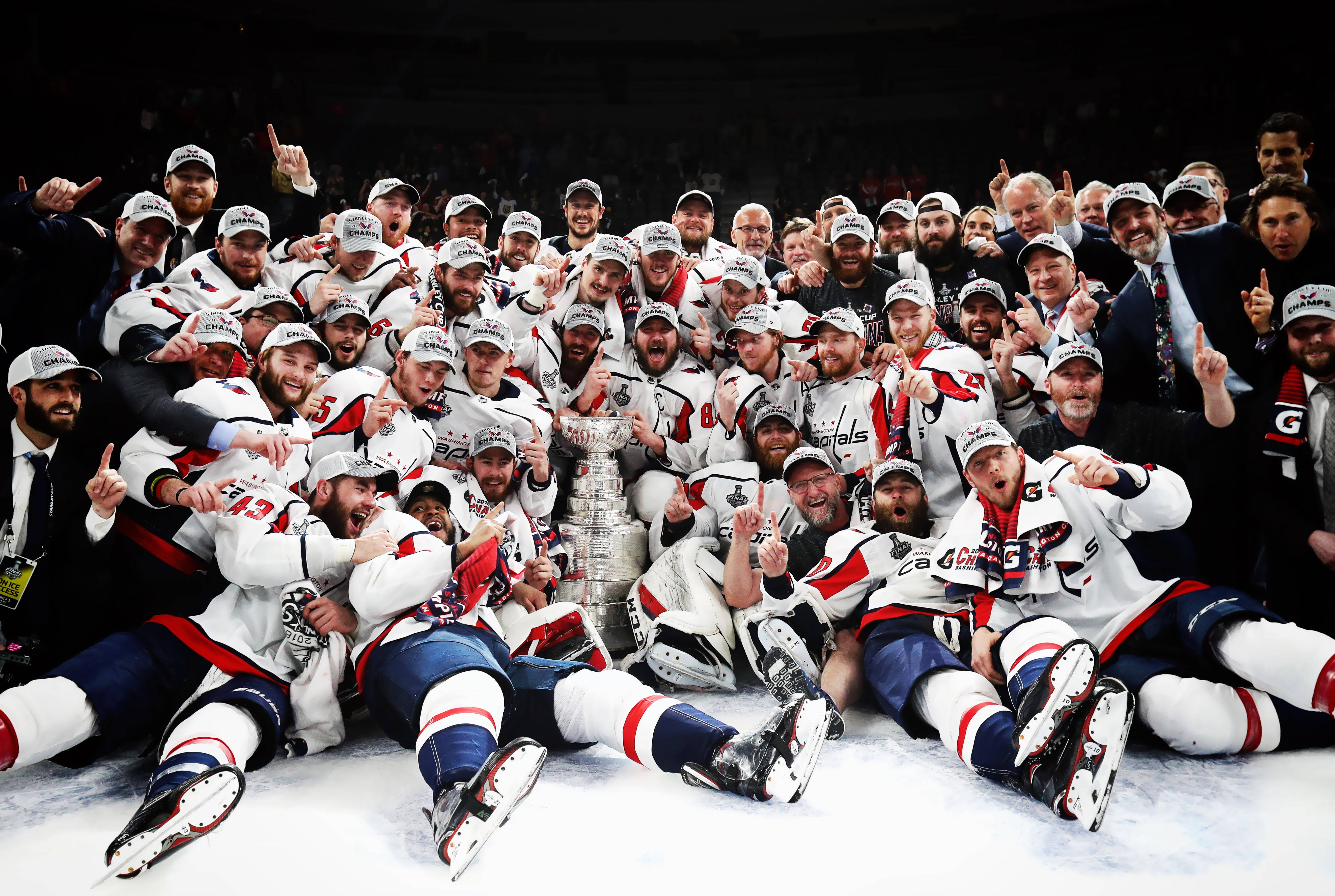 hockey 桌布 壁紙 — 冰球隊在冰上慶祝勝利，捧起史丹利盃，被身穿白色球衣的狂喜球員和工作人員包圍。