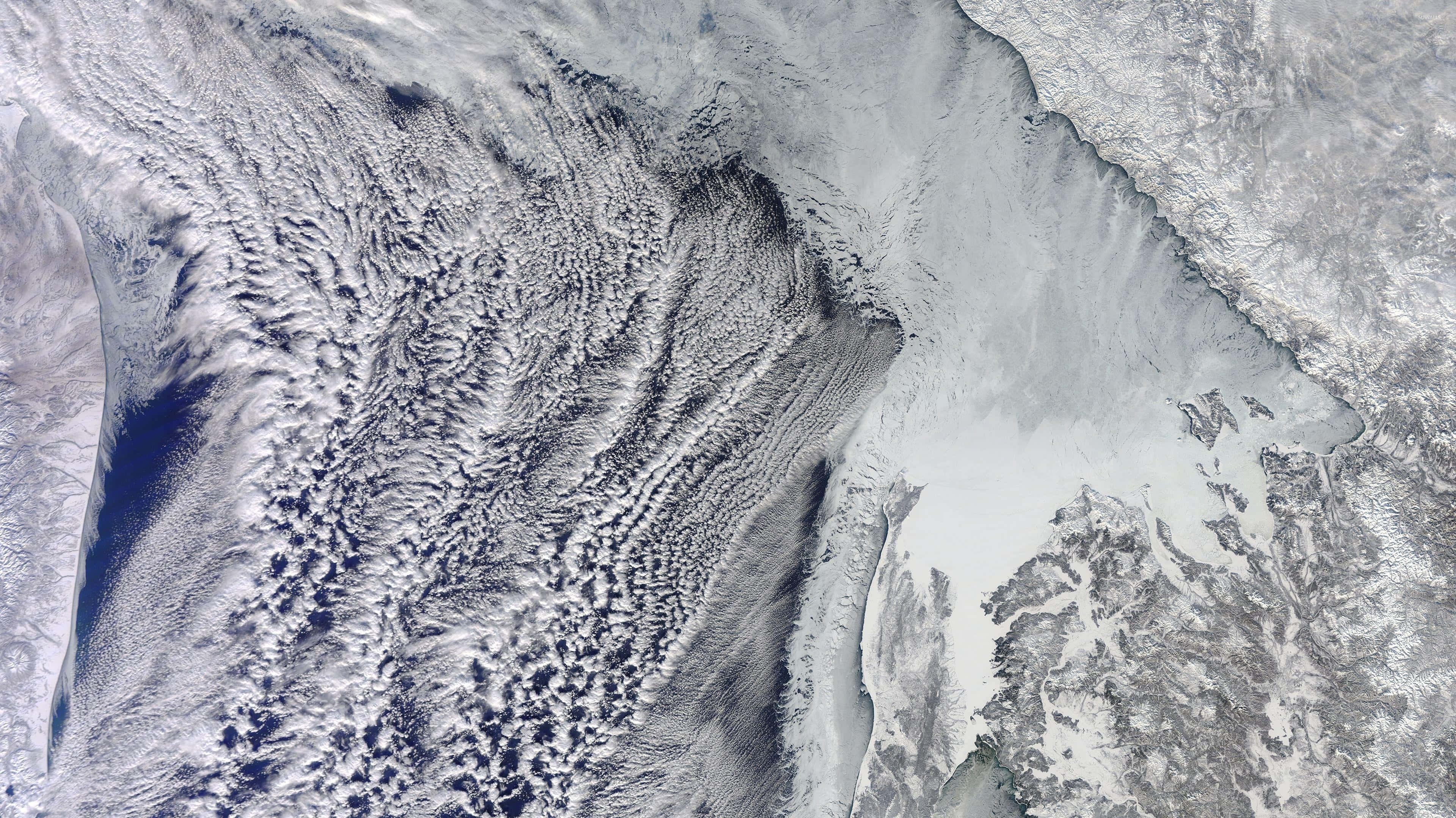 Satellite 桌布 壁紙 — 冰藍色水域和白雪覆蓋的陸地上空旋轉白雲的航空衛星視圖。