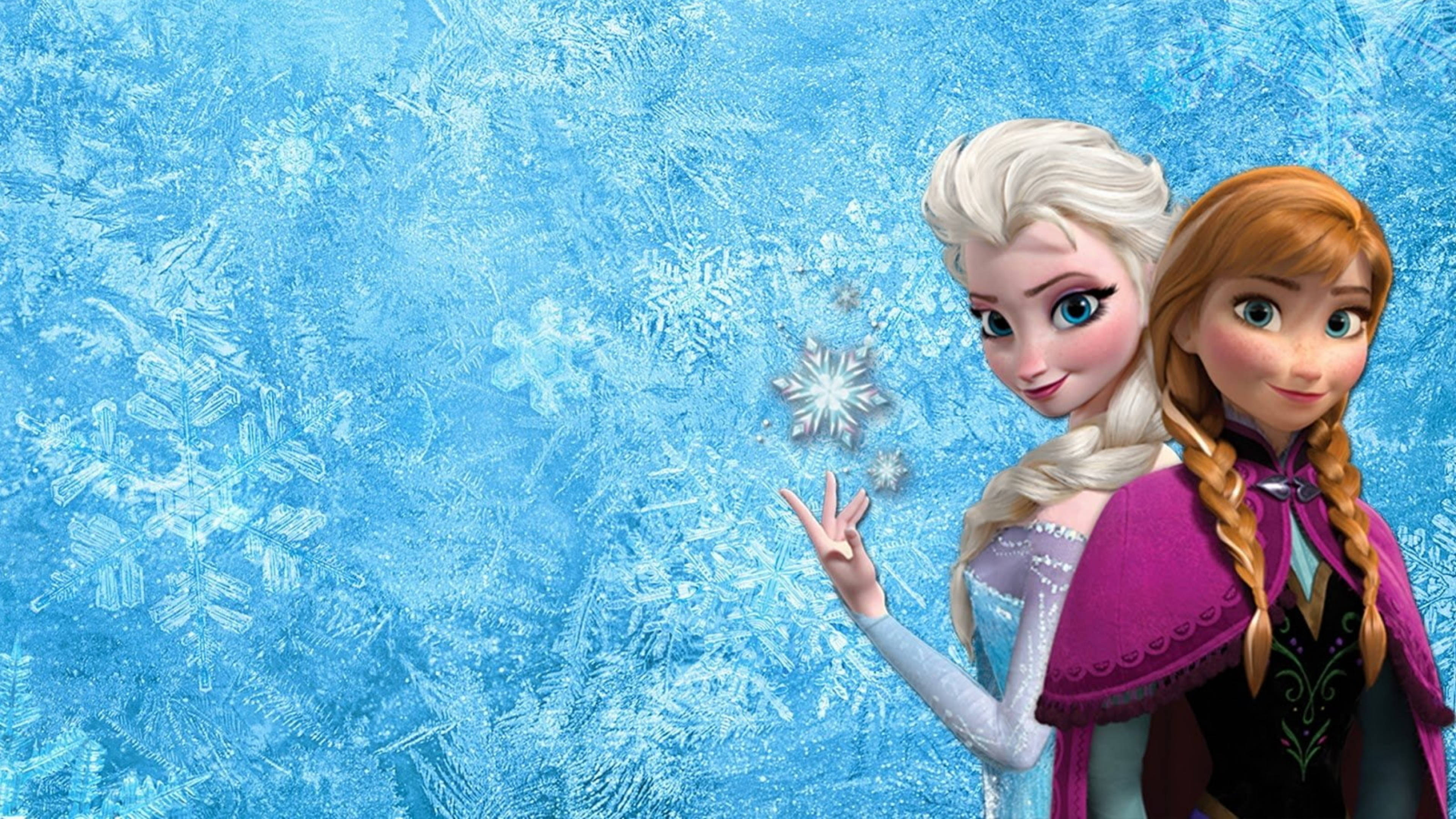 Frozen Elsa 桌布 壁紙 — 《冰雪奇緣》的艾莎和安娜站在閃爍的冰藍色背景前，背景有霜花圖案和飄浮的雪花。
