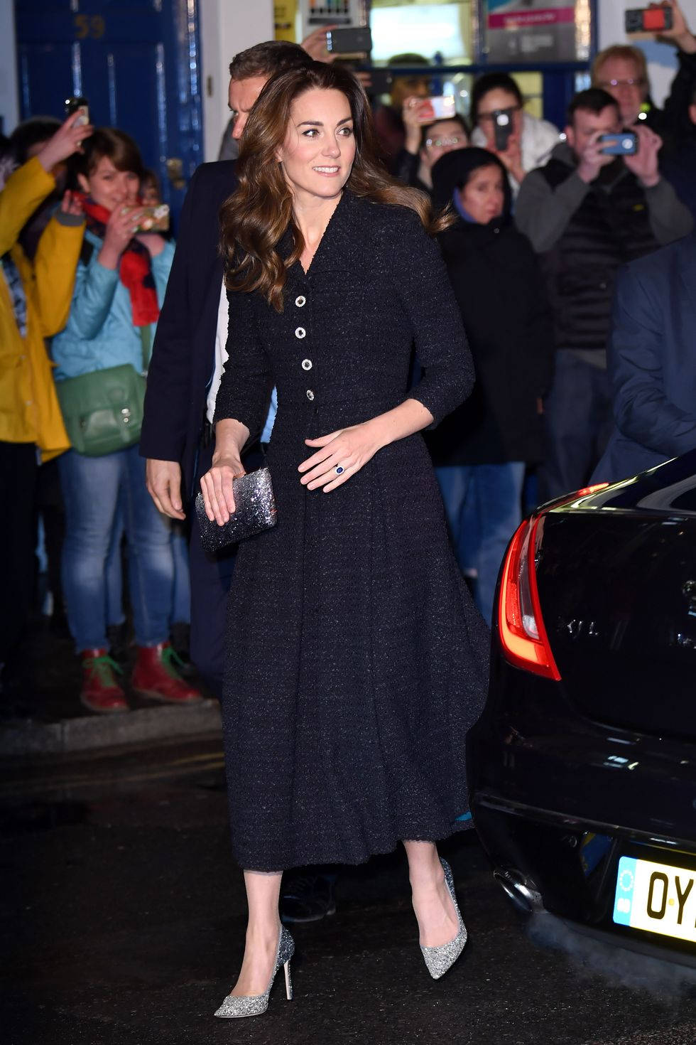 Kate Middleton 桌布 壁紙 — 凱特·米德爾頓自信地穿著深色粗花呢外套和閃亮高跟鞋，粉絲和攝影師在夜晚捕捉她在建築物外的時刻。