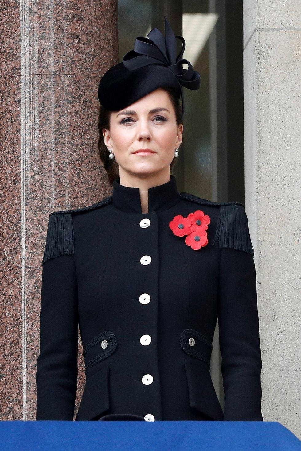 Kate Middleton 桌布 壁紙 — 凱瑟琳身穿黑色外套，飾有紅色罌粟花和相配的帽子，莊嚴地站在石陽台上。