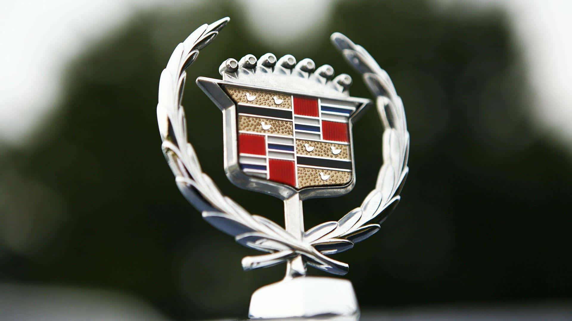 Car Logo 桌布 壁紙 — 凱迪拉克標誌特寫，帶有紅色、金色和藍色琺瑯細節，由銀色月桂花環環繞，背景為模糊的綠色。
