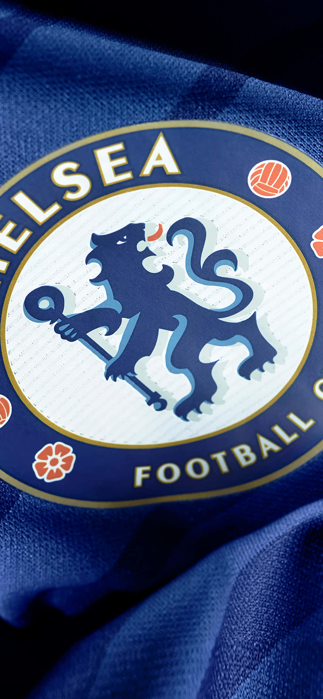 Chelsea iPhone 桌布 壁紙 — 切爾西足球俱樂部徽章特寫，位於有紋理的皇家藍色球衣布料上，帶有橙色花卉和足球點綴。