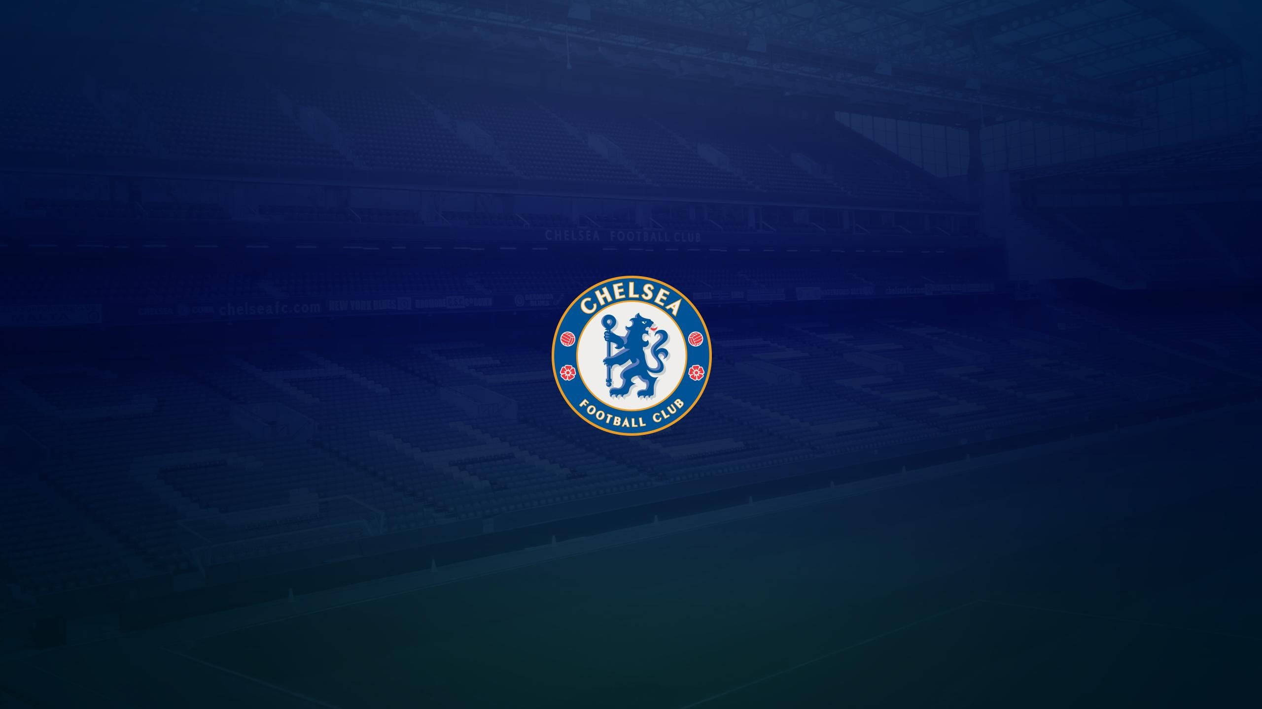 chelsea fc logo 桌布 壁紙 — 切爾西足球俱樂部標誌居中於燈光昏暗、藍色色調且空無一人的球場。