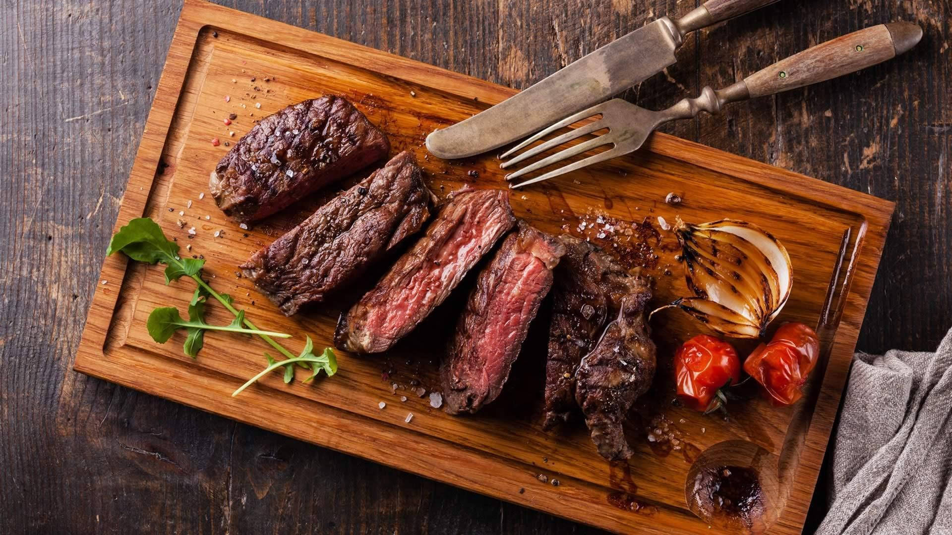 meat 桌布 壁紙 — 切片中等熟度牛排搭配烤櫻桃番茄和大蒜，放在質樸的木砧板上。