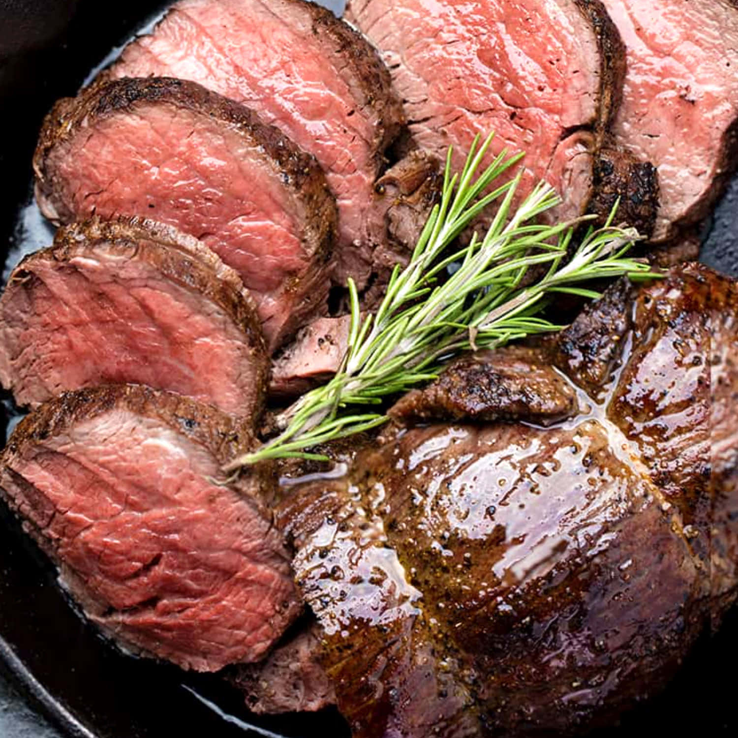 meat 桌布 壁紙 — 切片中等熟度的牛肉配迷迭香裝飾，在鑄鐵煎鍋中閃閃發光。