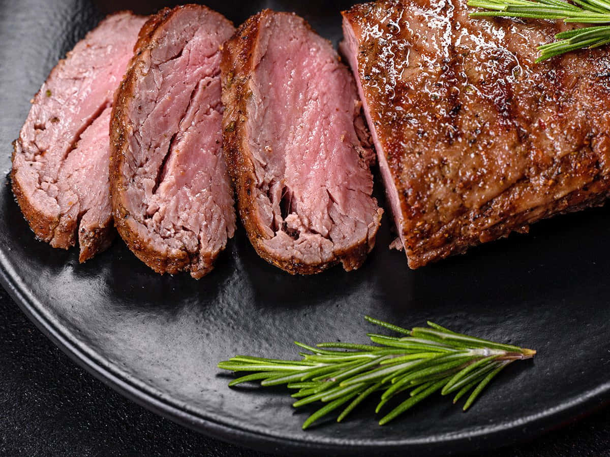 meat 桌布 壁紙 — 切片五成熟牛肉佐迷迭香裝飾，置於霧面黑色餐盤上。