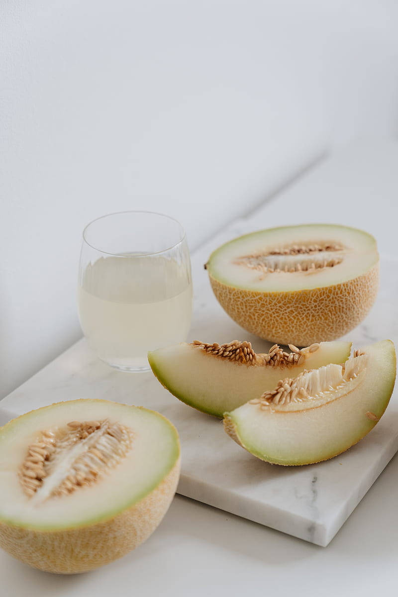 Fruits 桌布 壁紙 — 切片哈密瓜和一杯水放在白色大理石砧板上，背景是簡約的白色。