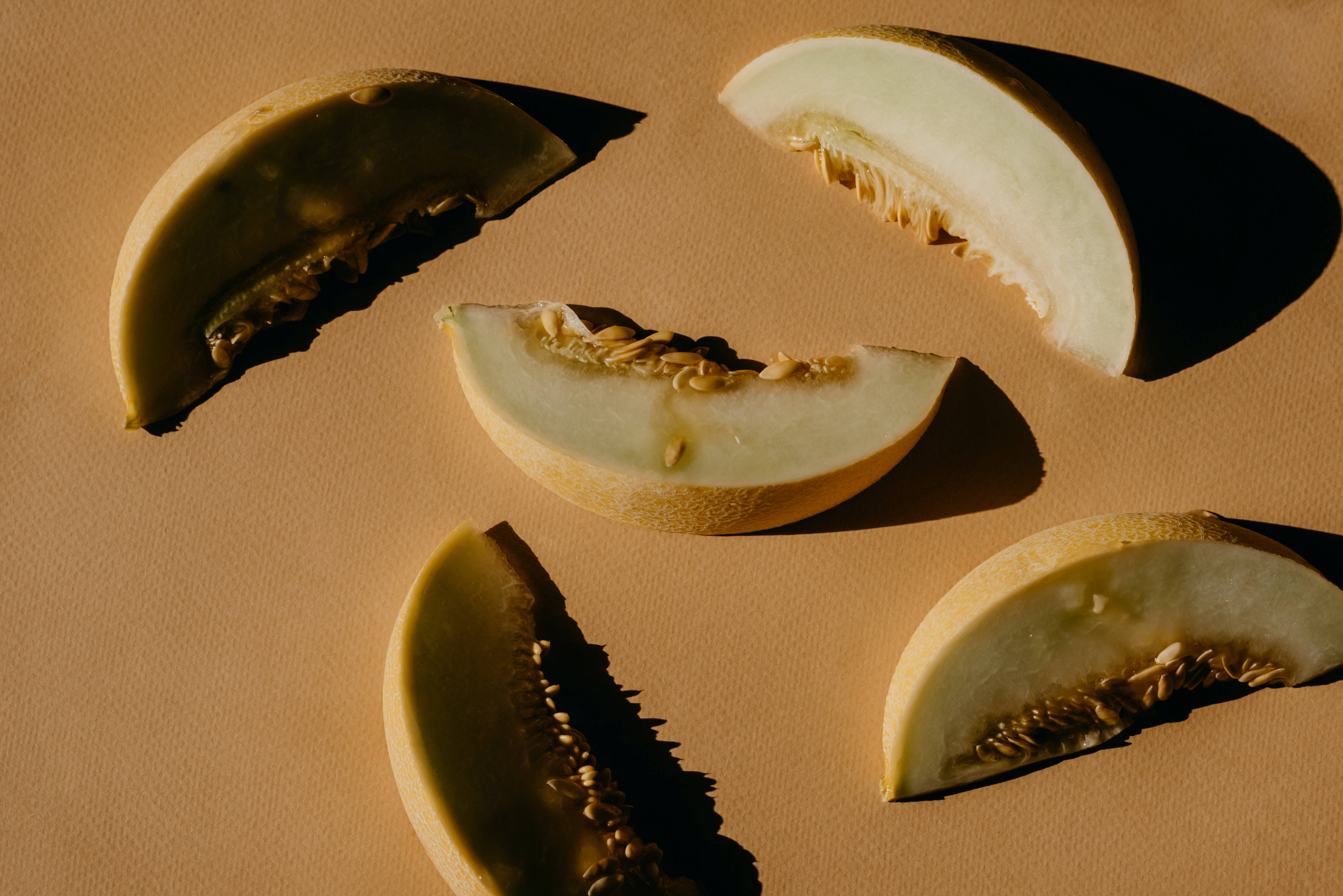 Fruits 桌布 壁紙 — 切片哈密瓜塊排列在溫暖的米色表面上，帶有定向照明產生的戲劇性陰影。