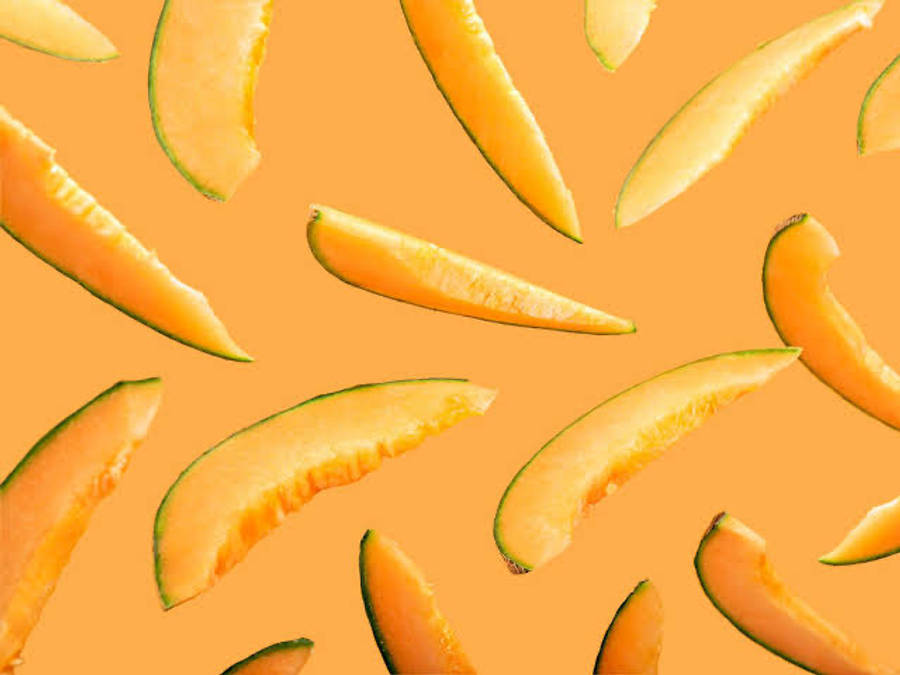 Fruit 桌布 壁紙 — 切片哈密瓜果肉在溫暖的橙色背景上漂浮，形成充滿活力的熱帶圖案。