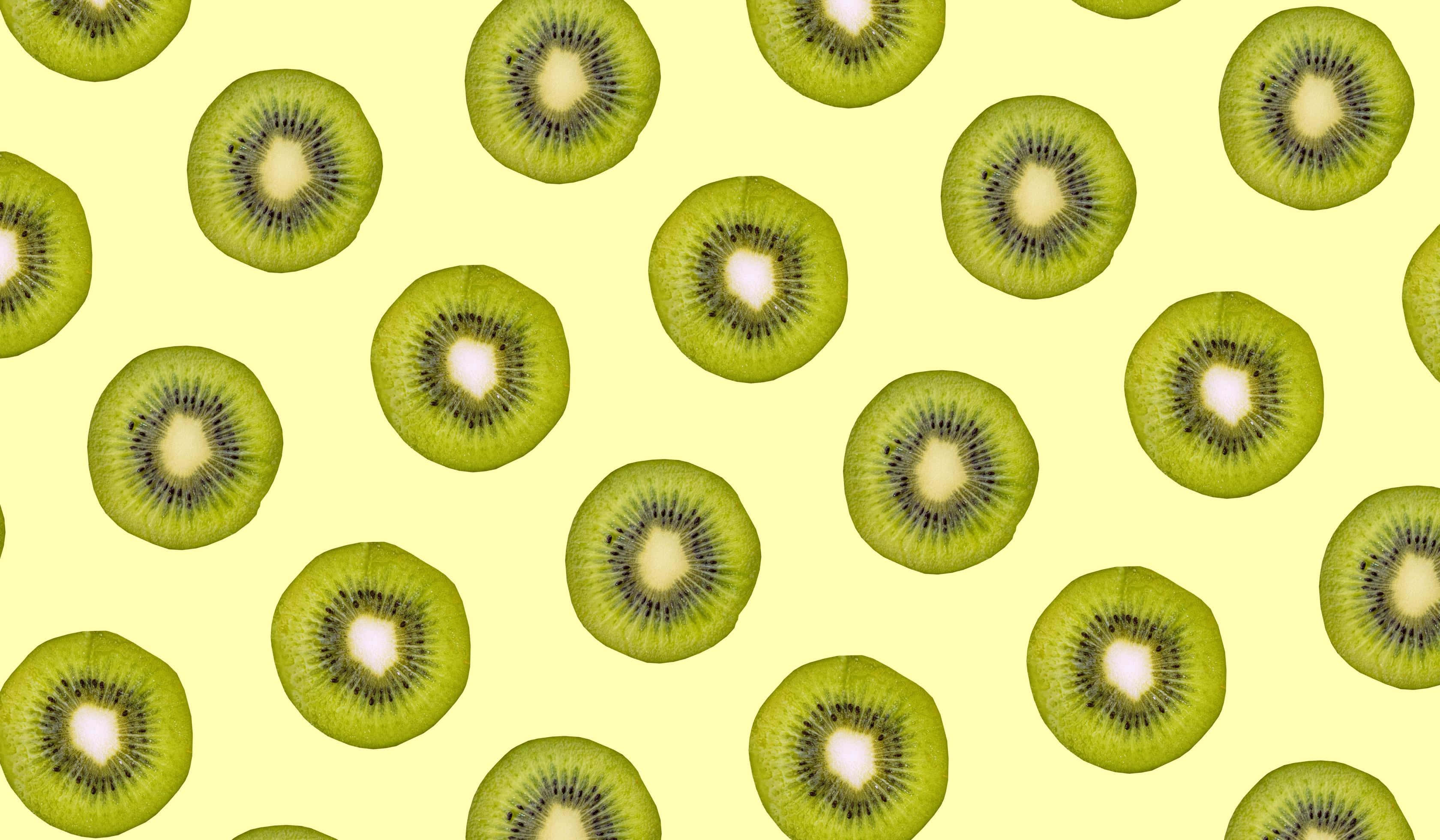 Kiwi 桌布 壁紙 — 切片奇異果以重複圖案排列在淡黃色背景上。