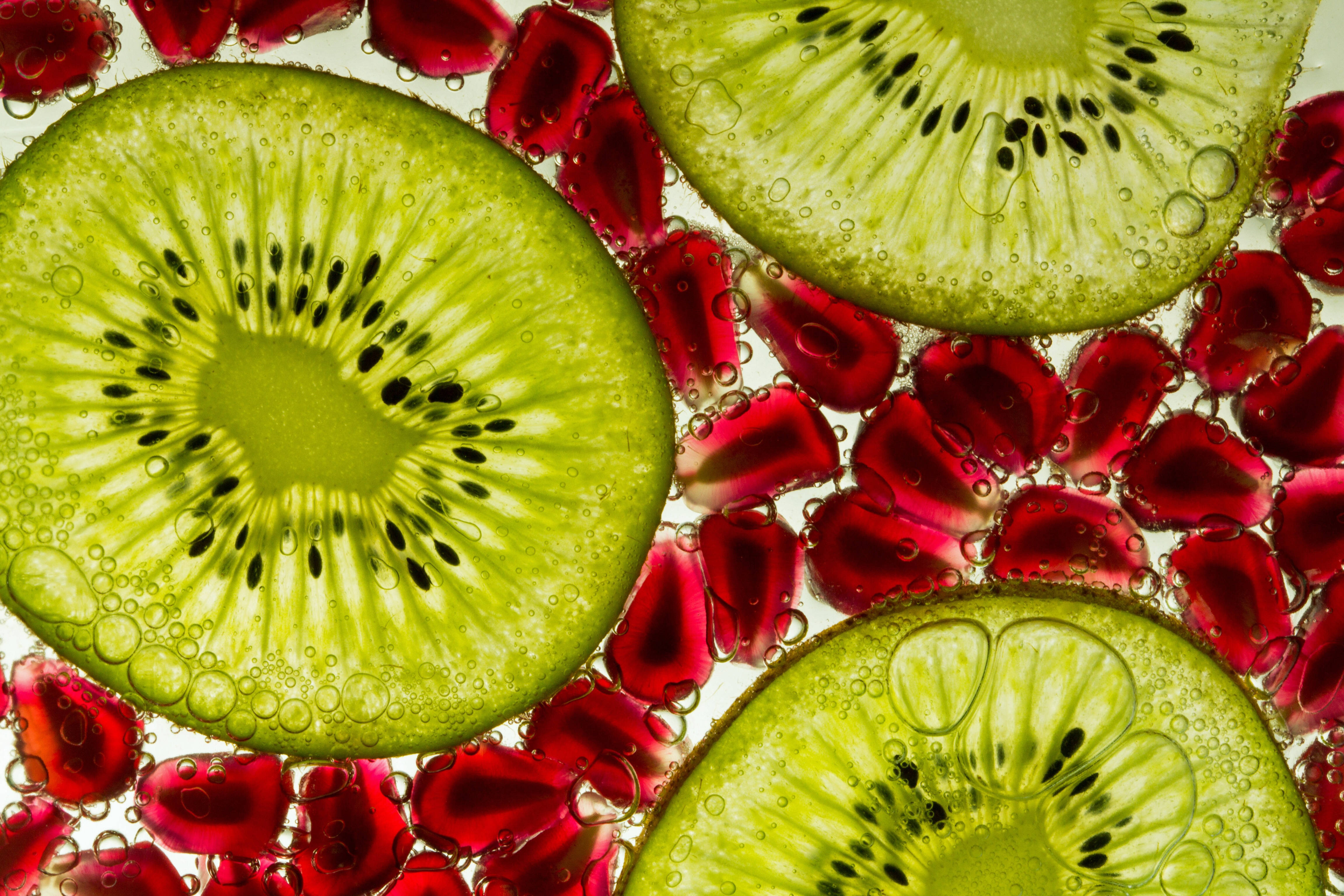 Fruits 桌布 壁紙 — 切片奇異果和石榴籽漂浮在氣泡水中，營造出充滿活力、多汁的抽象構圖。
