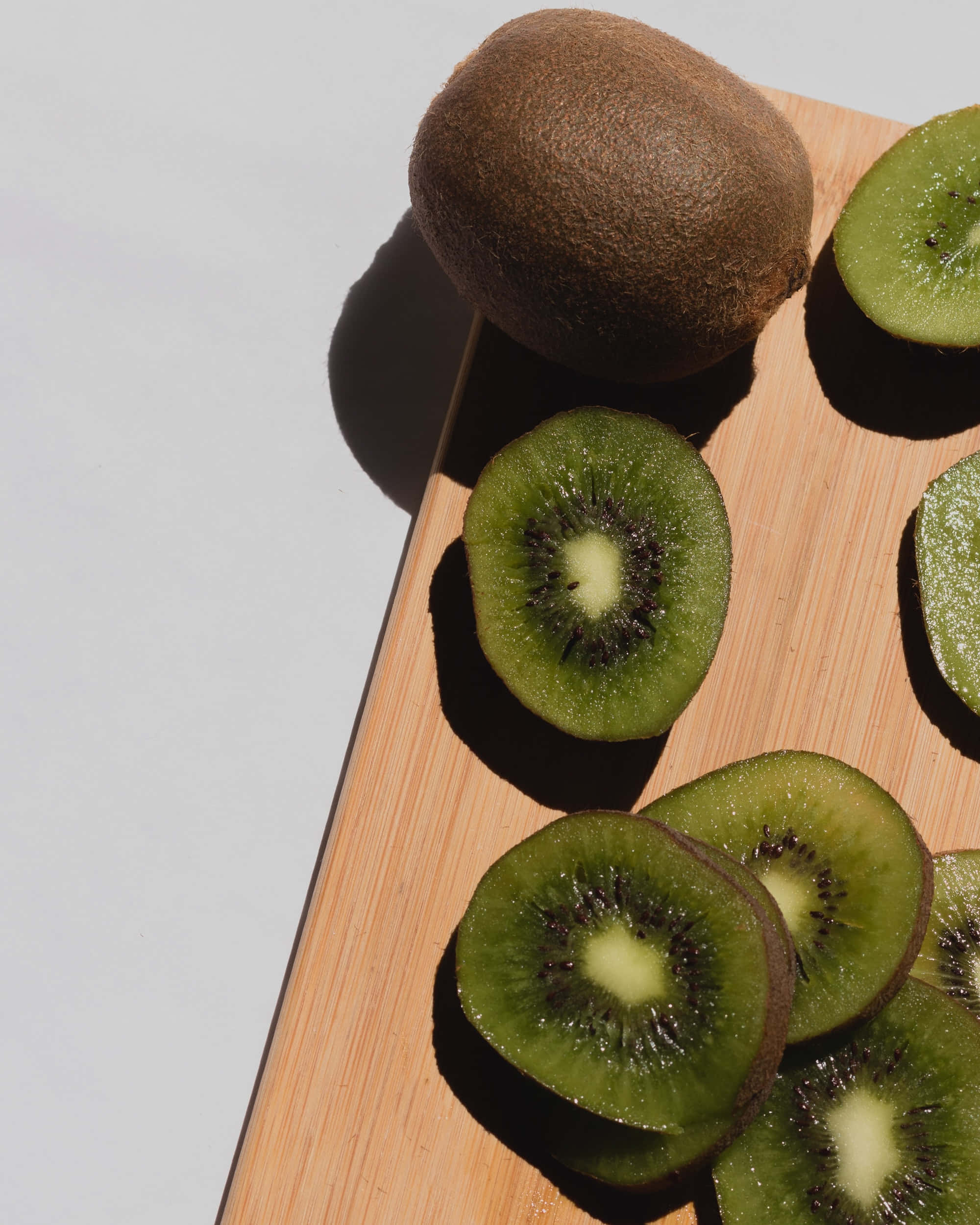 Fruit 桌布 壁紙 — 切片奇異果帶有絨毛棕色外皮和鮮綠色果肉，在明亮陽光下放在木製砧板上。