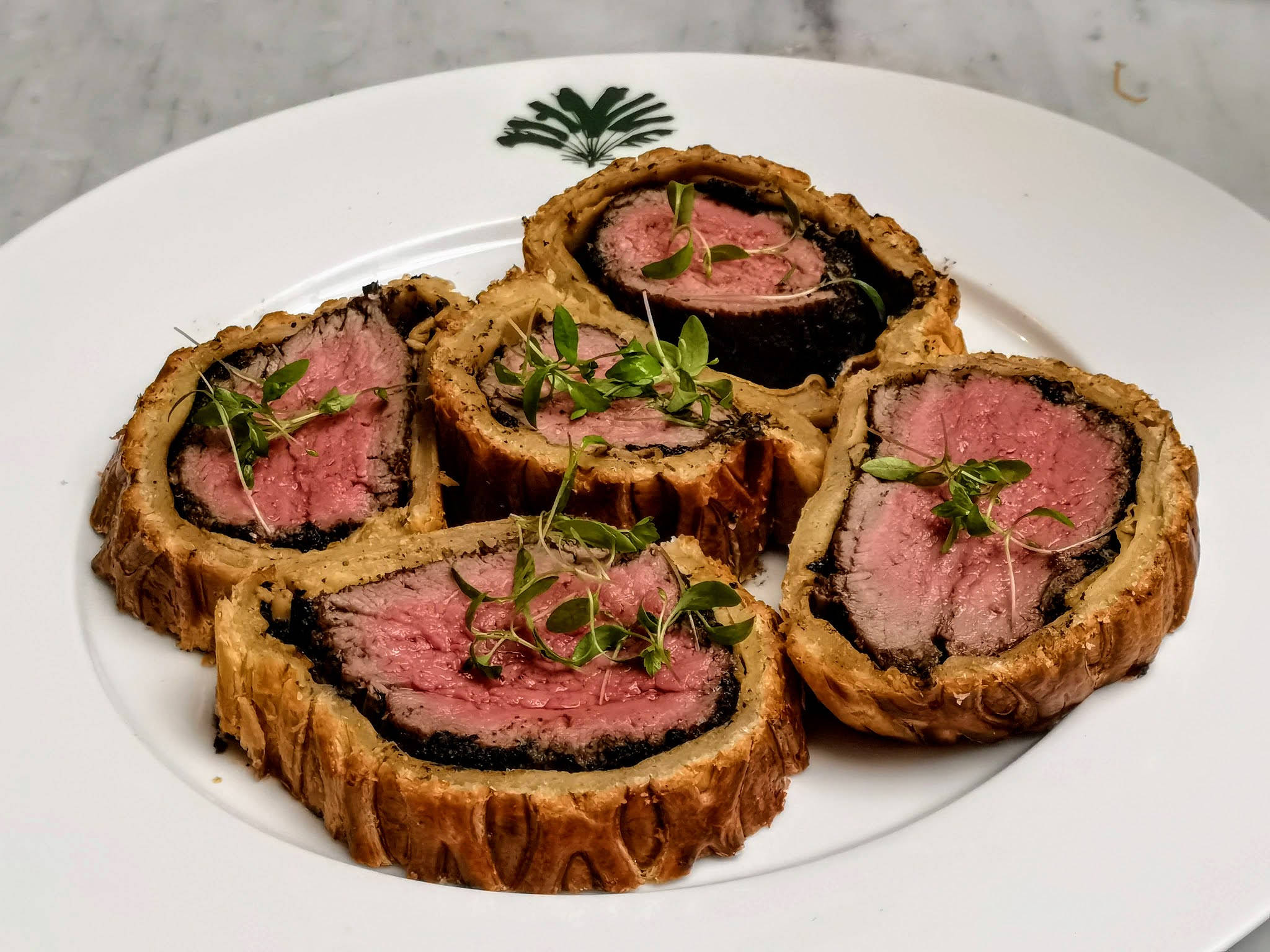meat 桌布 壁紙 — 切片威靈頓牛排搭配金黃外皮和新鮮香草，盛放在白色盤子上。