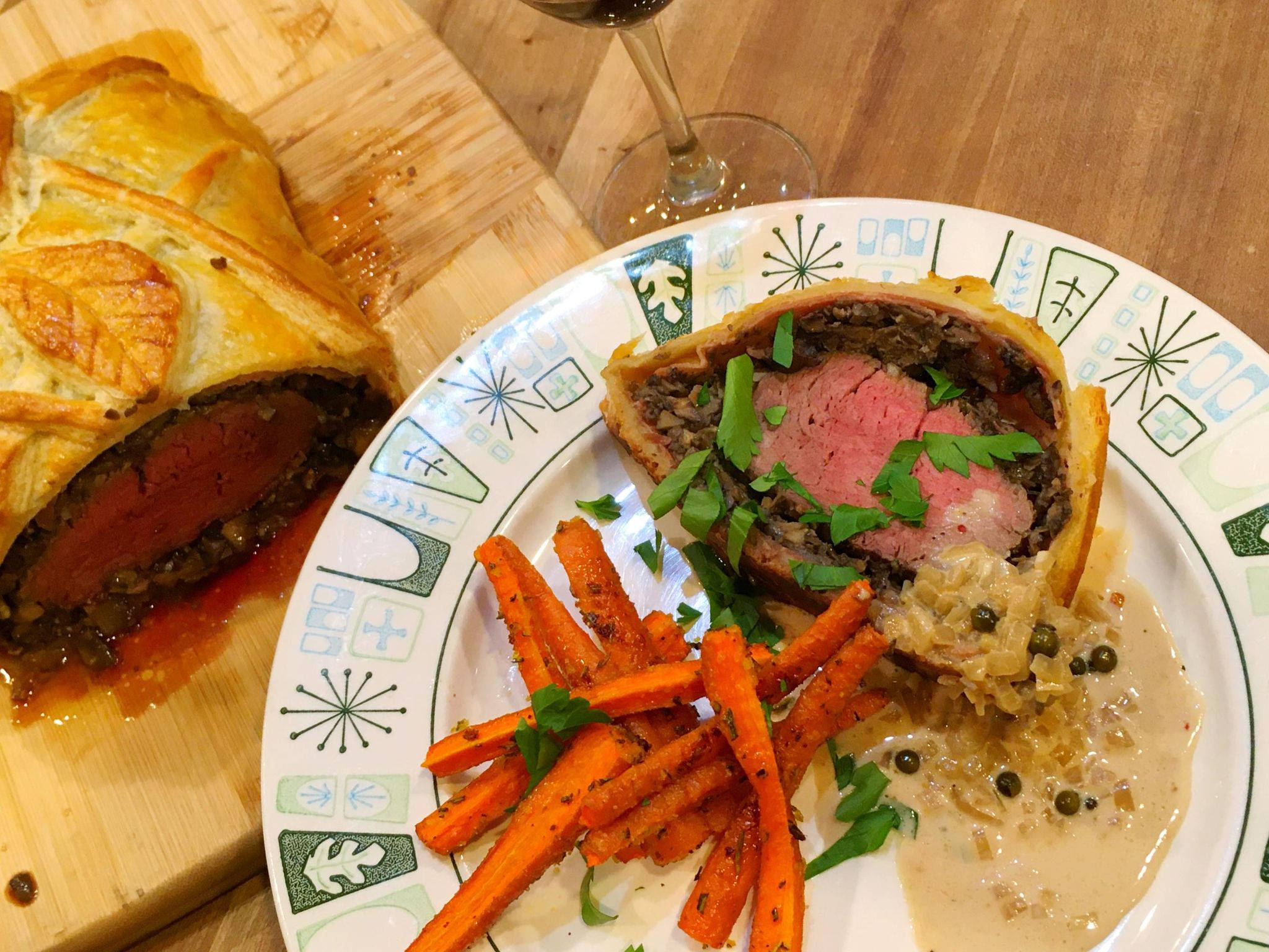 meat 桌布 壁紙 — 切片威靈頓牛排搭配金黃酥皮和香草裝飾，放在圖案盤上，旁邊有烤胡蘿蔔和奶油醬。